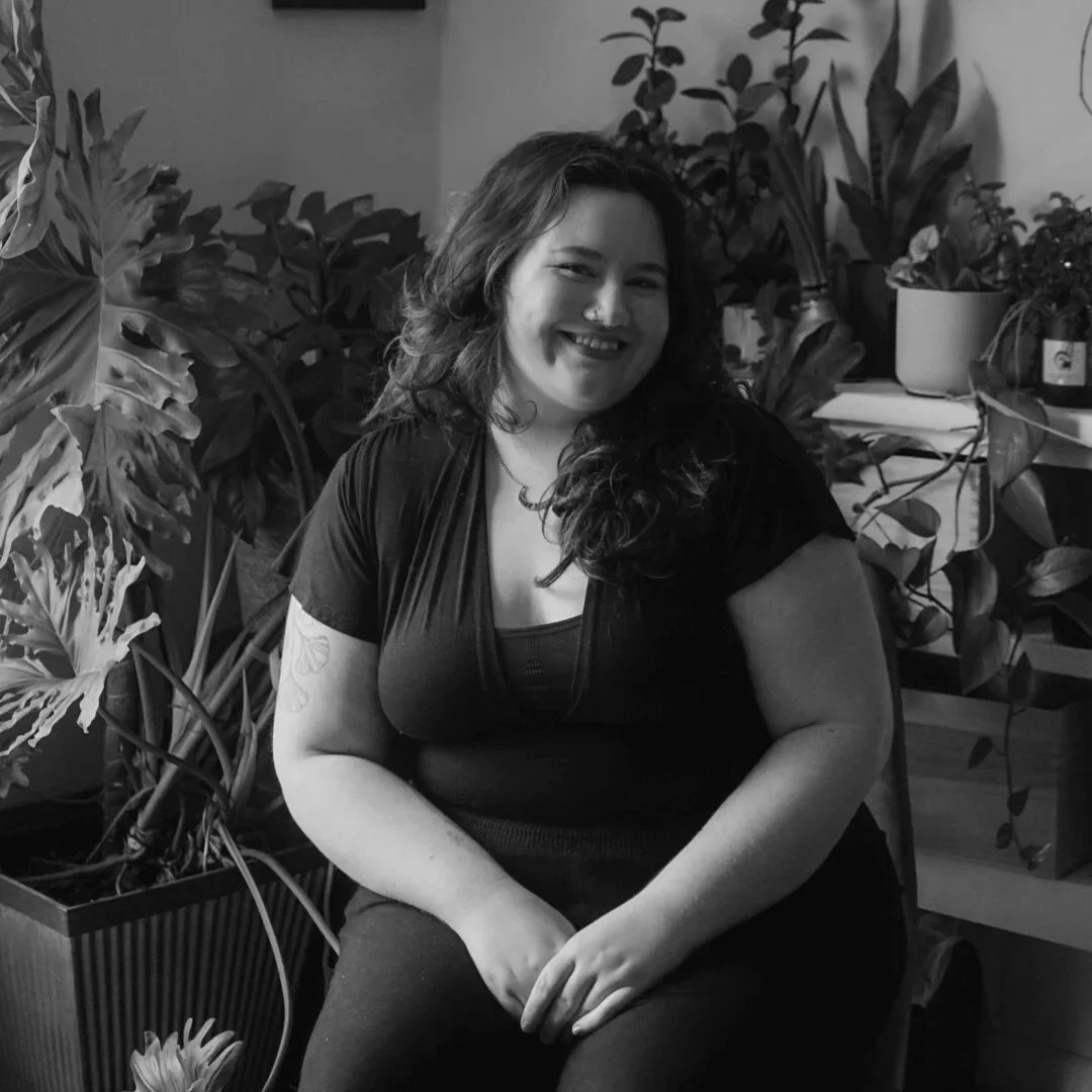 A woman sitting amid houseplants, smiling at the camera in a black and white photo.