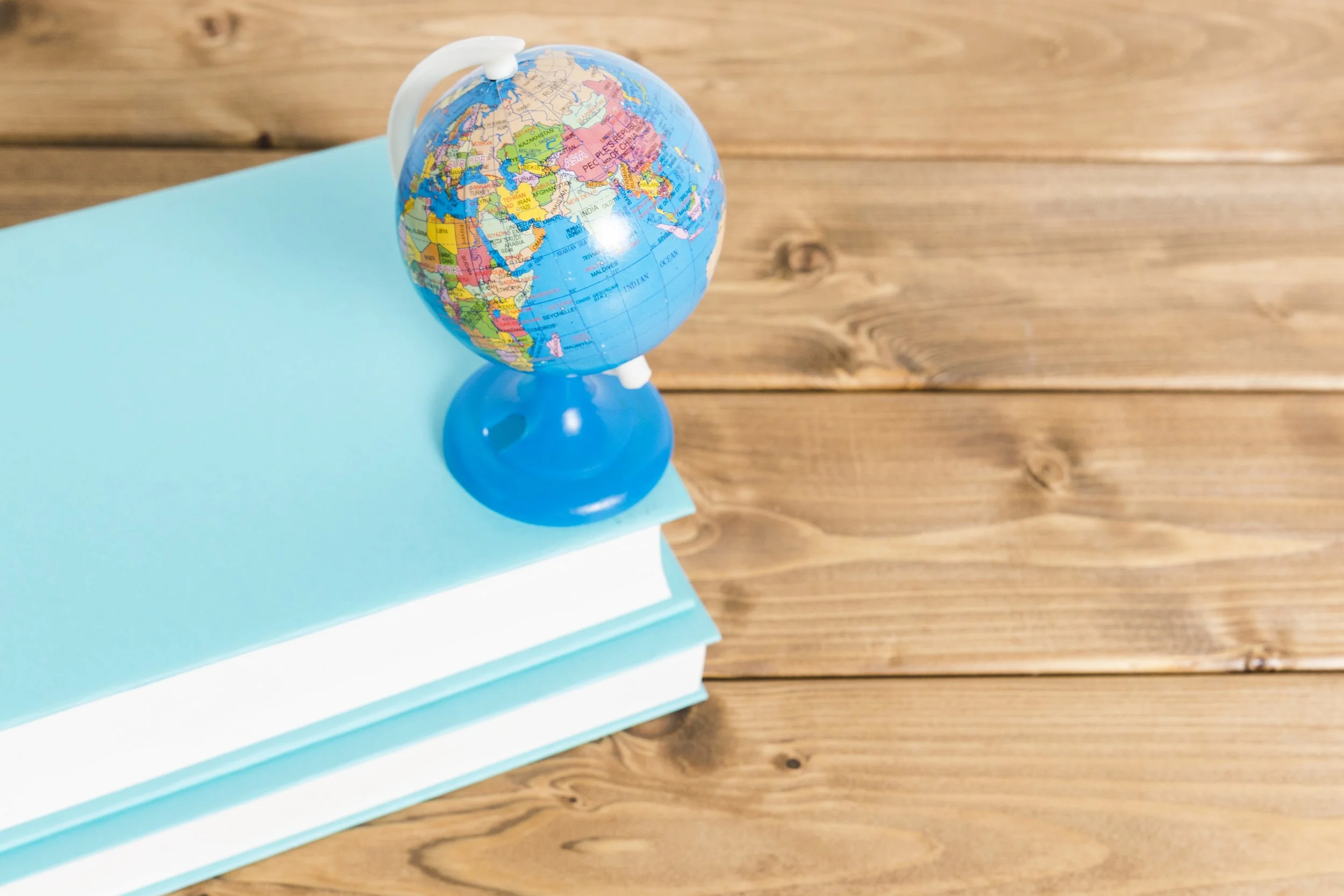 A small globe resting on stacked light blue notebooks on a wooden surface.