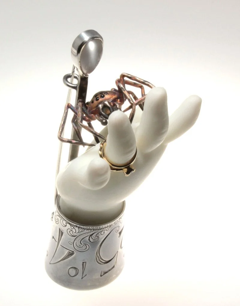 A brooch in the form of a hand set in a silver cuff, with a spider holding the wedding ring 