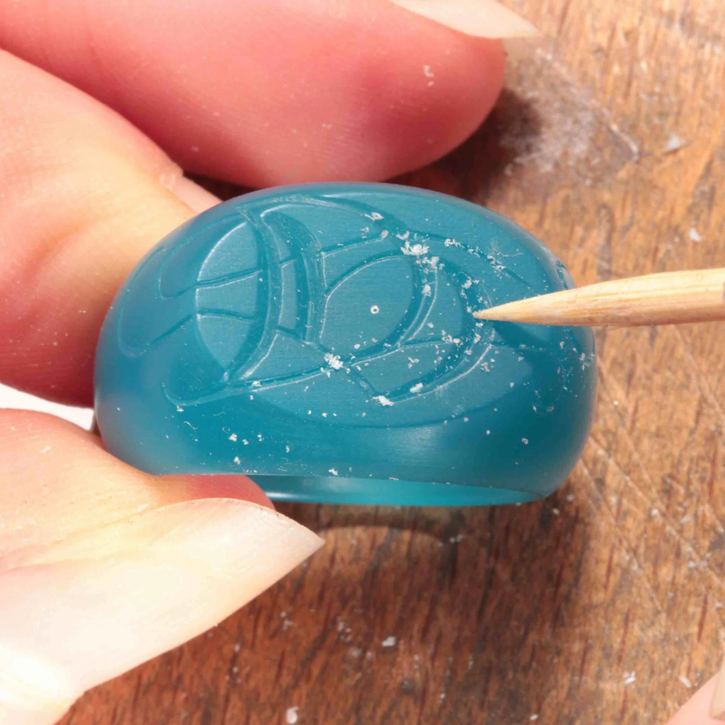 Fingers holding a hand carved wax model of a signet ring with carved monogram