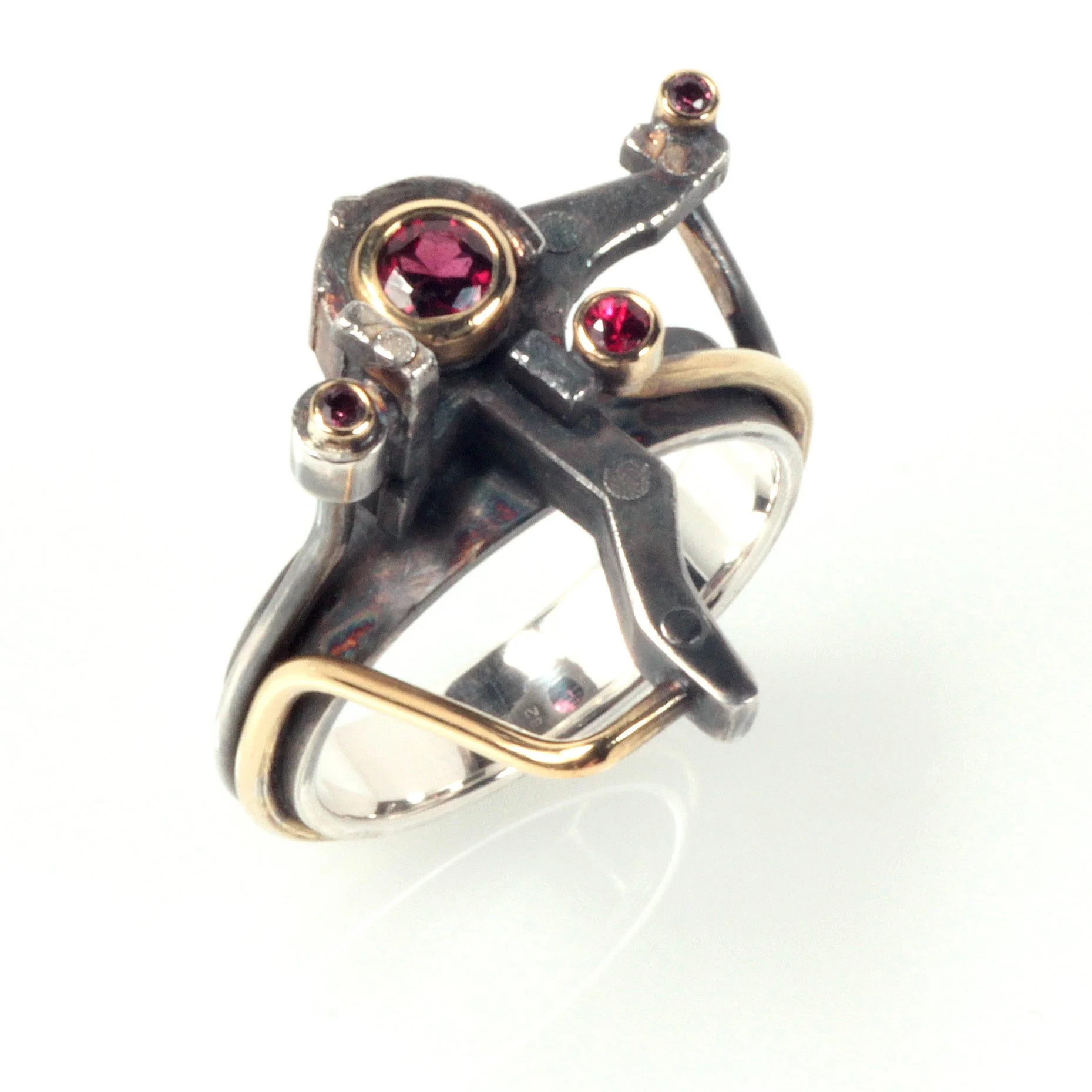 An oxidised silver and gold ring set with red gemstones