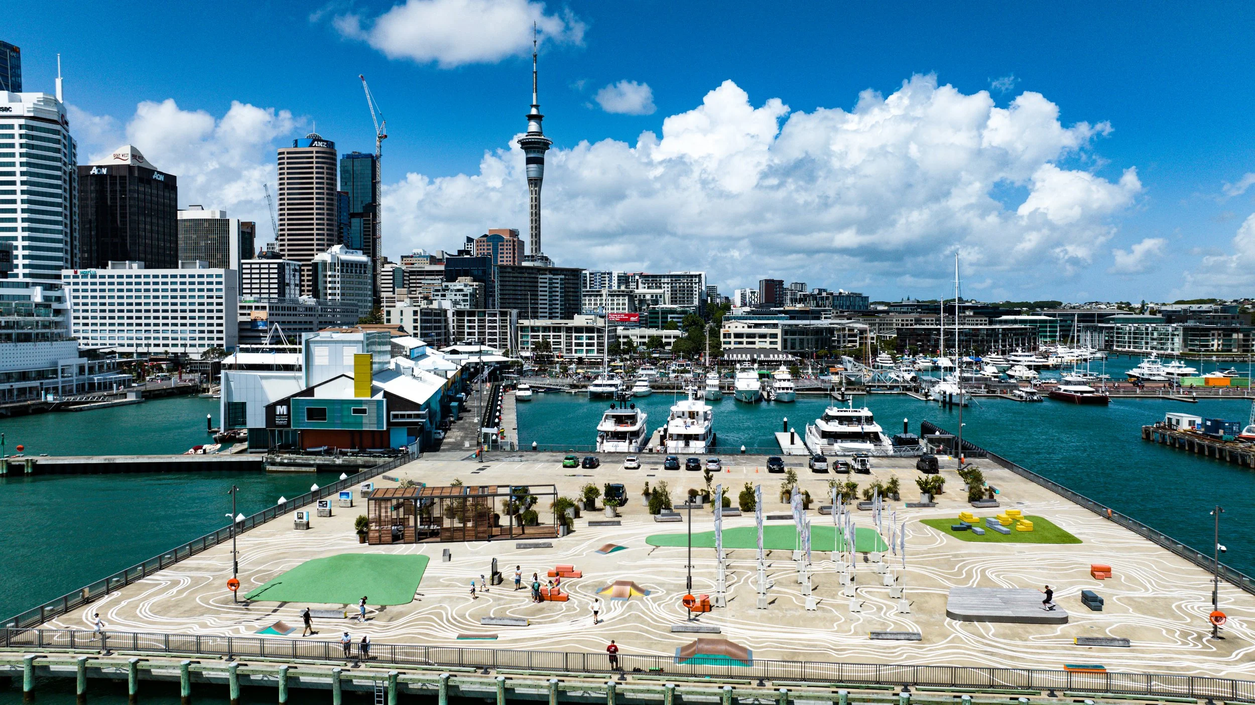 Sydney waterfront with boats docked at the marina, city skyscrapers in the background, and a landscaped outdoor area with walking paths and seating