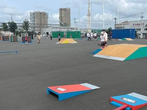 Outdoor skatepark with ramps, rails, and people. Urban background with buildings and communication towers.