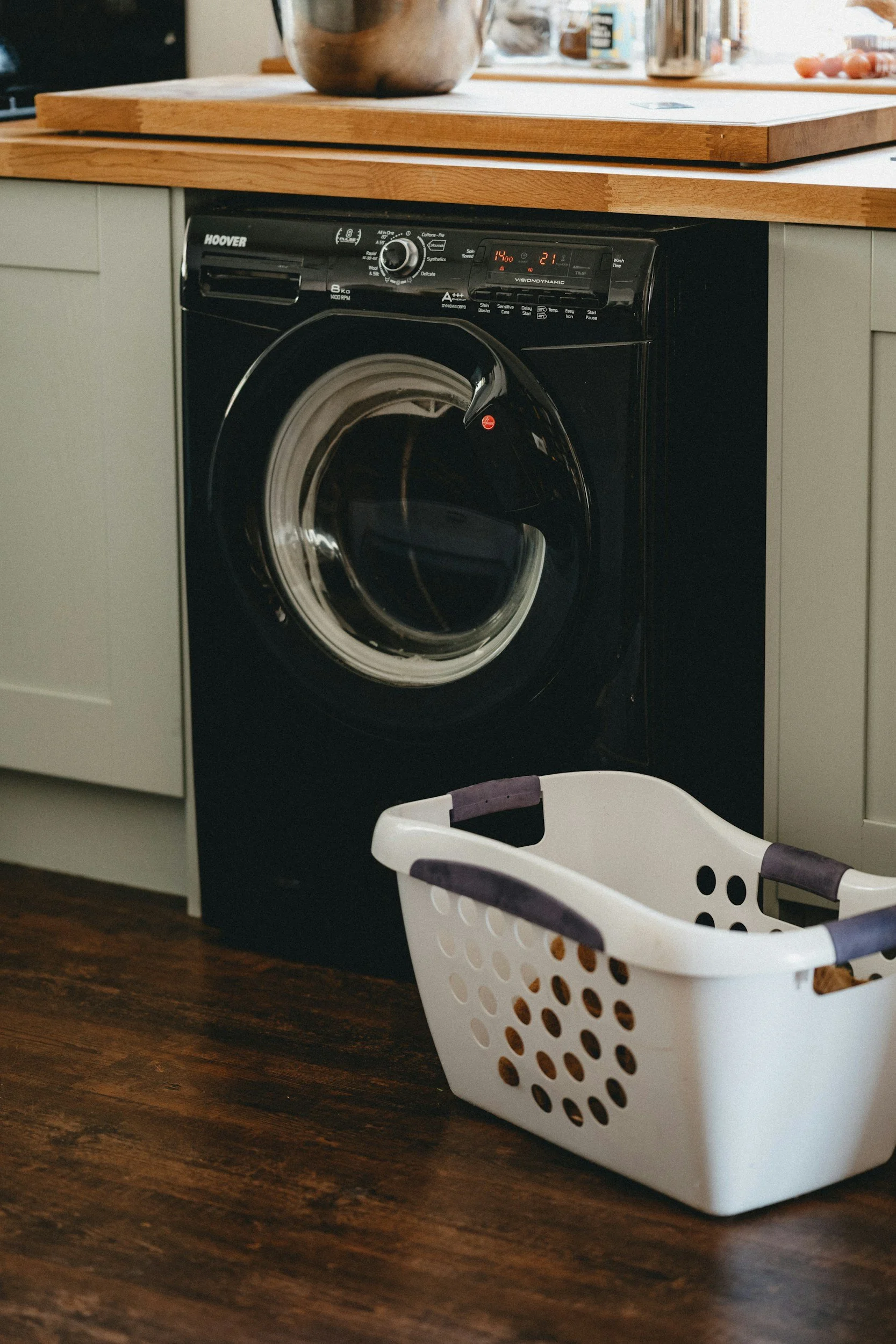 A laundry area with a washing machine, a laundry basket, and a countertop in a kitchen or laundry room.