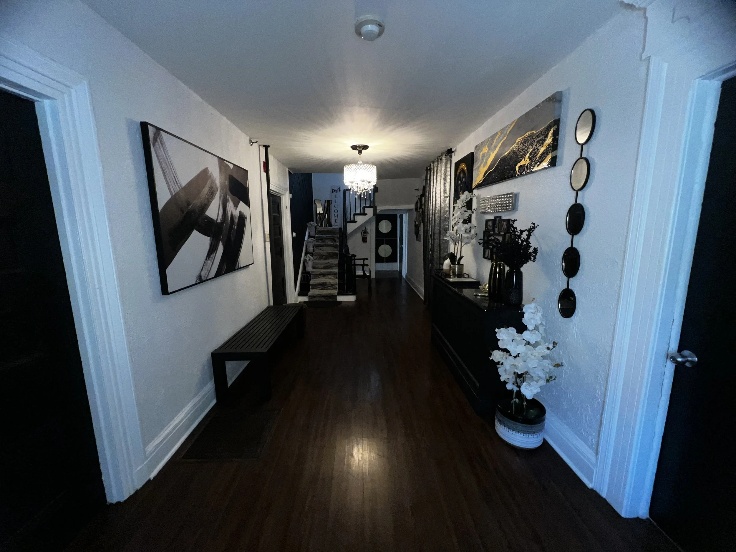 Hallway with white walls, dark wooden floor, artwork, a chandelier, and decorative elements.