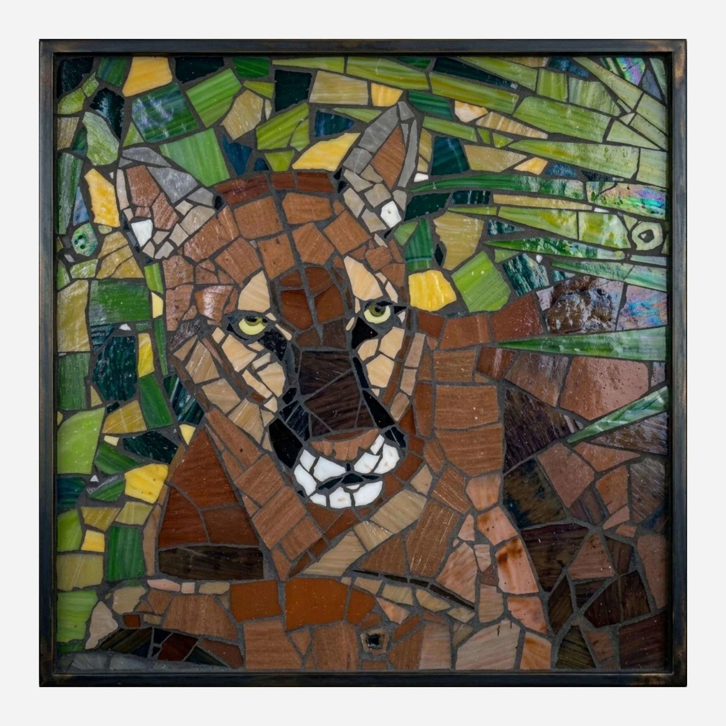 A mosaic of a mountain lion's face, with its front paws folded, made from colorful pieces of glass.