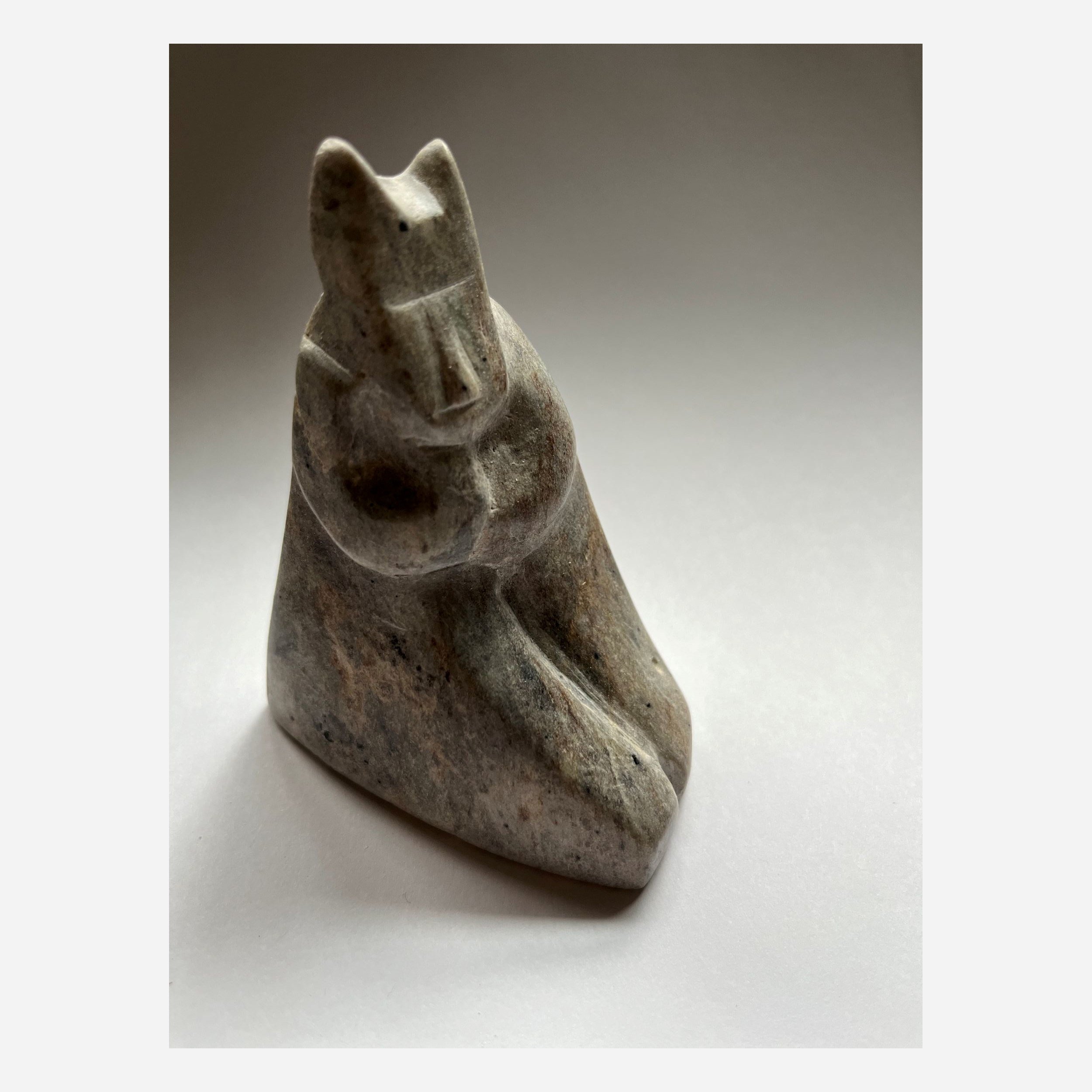 A hand carved figurine of an old cat sitting on its haunches