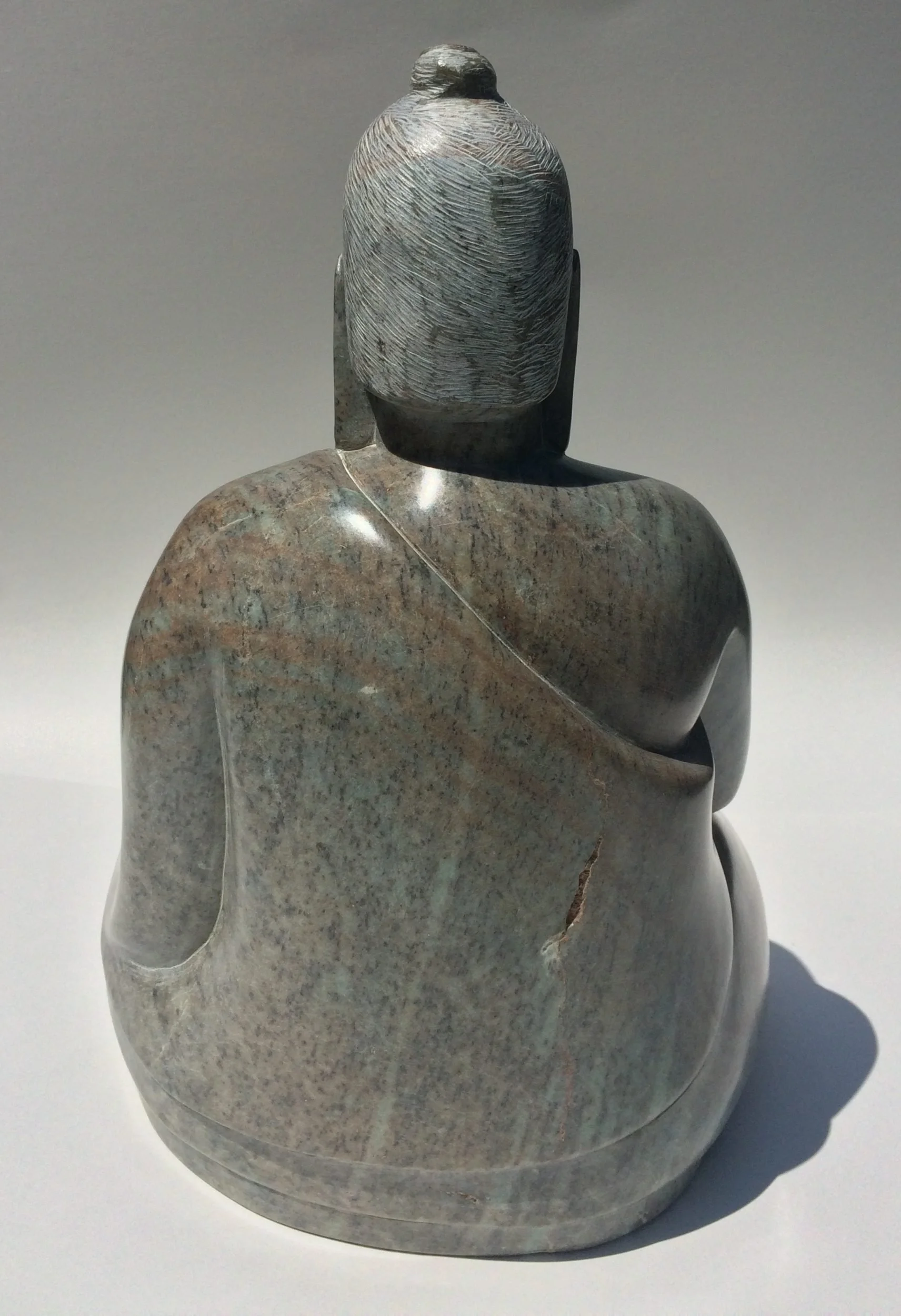 Rear view of a carving of the Buddha sitting with one hand touching the earth, hand carved from green Brazilian talc
