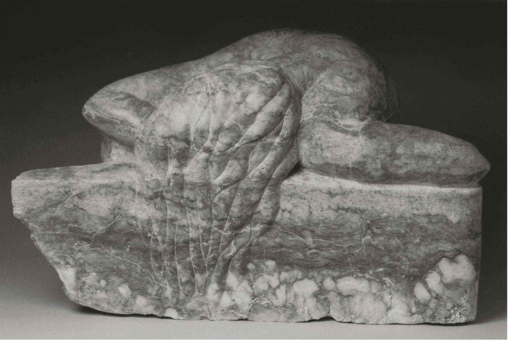 Alabster stone carving of a woman lying on a wall, with her hair cascading over its front.