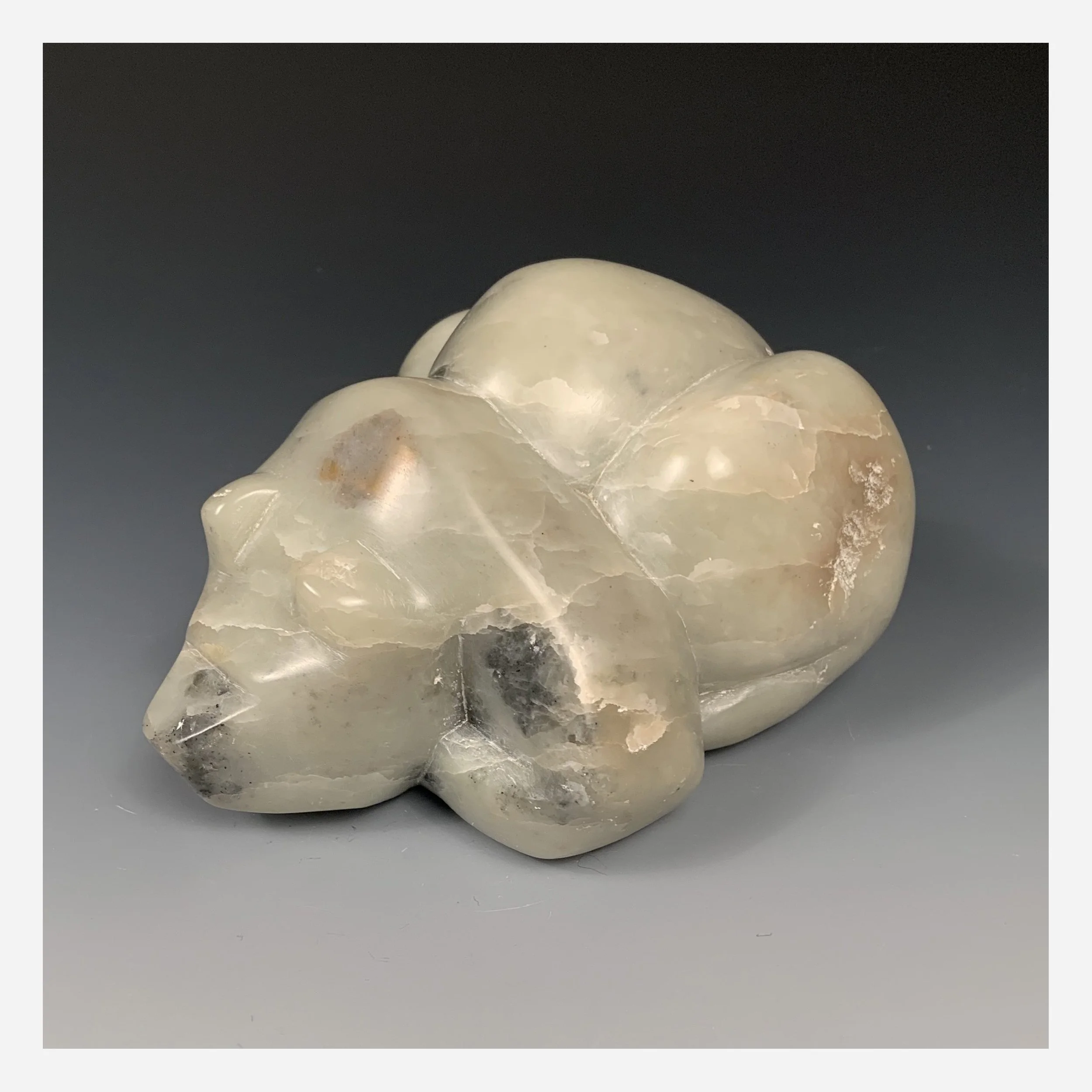 Profile of a hand crafted figure of a bear lying down, carved from green soapstone