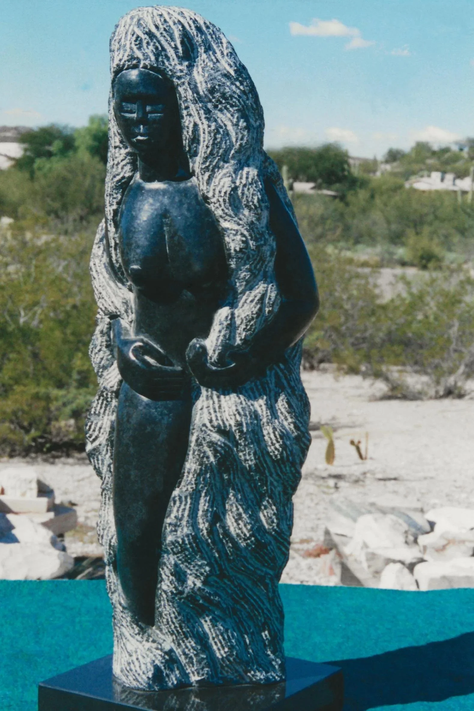 A large sculpted figure hand carved from black polished soapstone, set in a desert landscape.