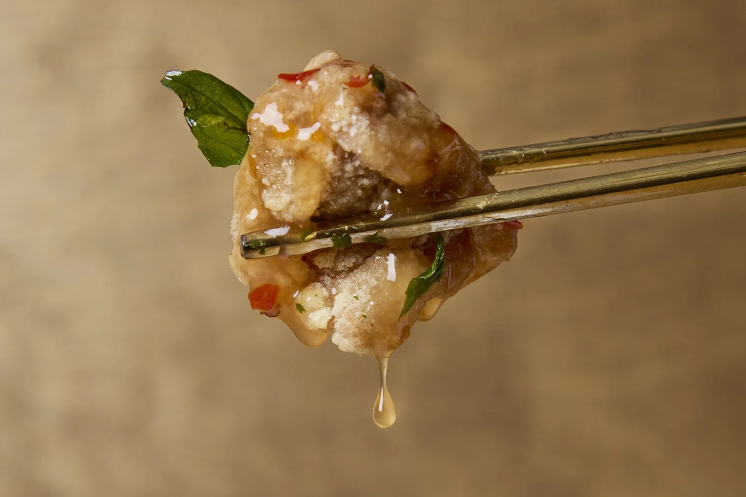 Lucky Lily in Vancouver Airport delicious fried chicken fried held by chopsticks, garnished with a green leaf and drizzled with sauce, with a droplet of sauce hanging from the food.