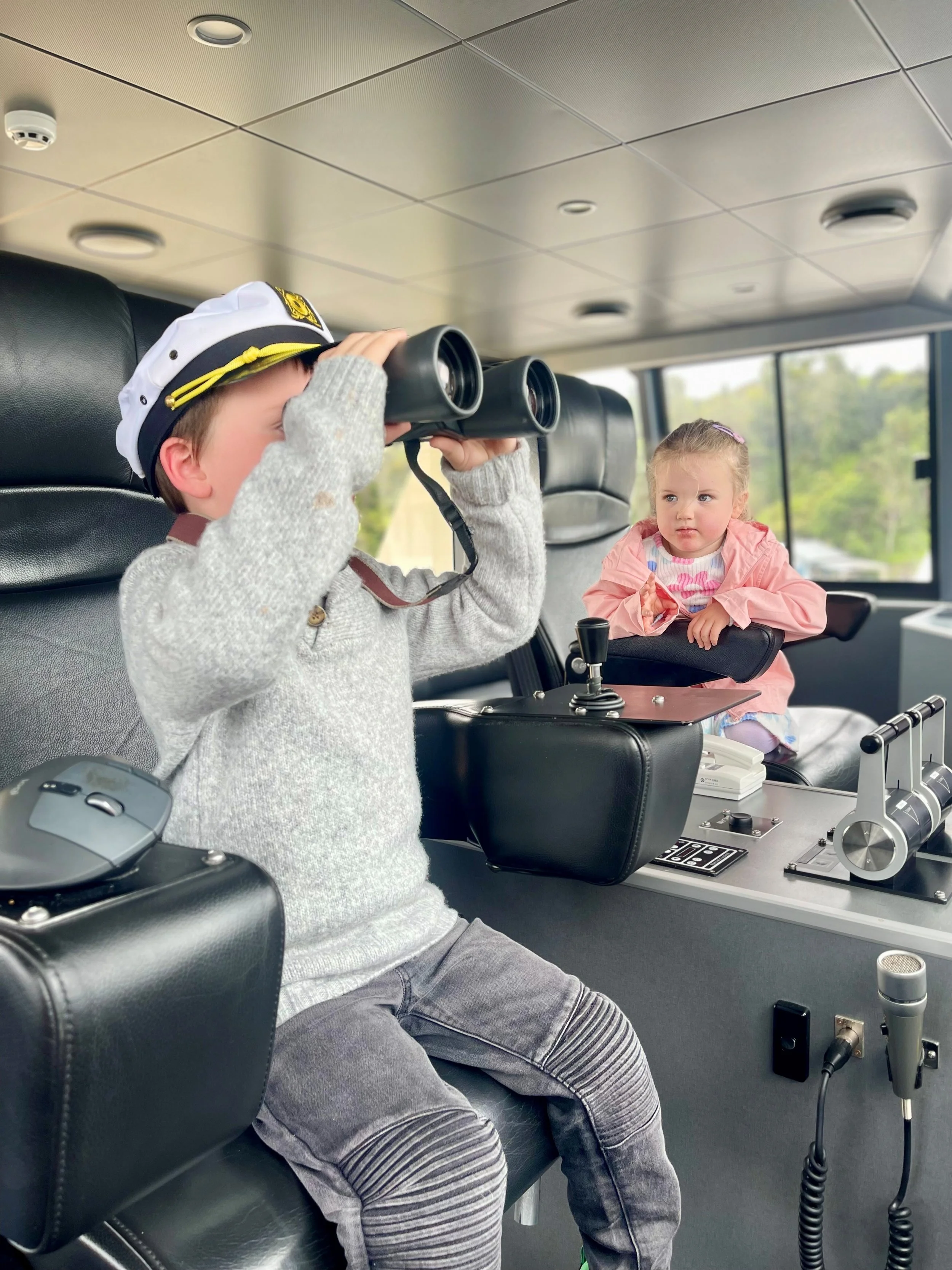 Child in wheelhouse of boat wearing a captains hat and looking through binoculars