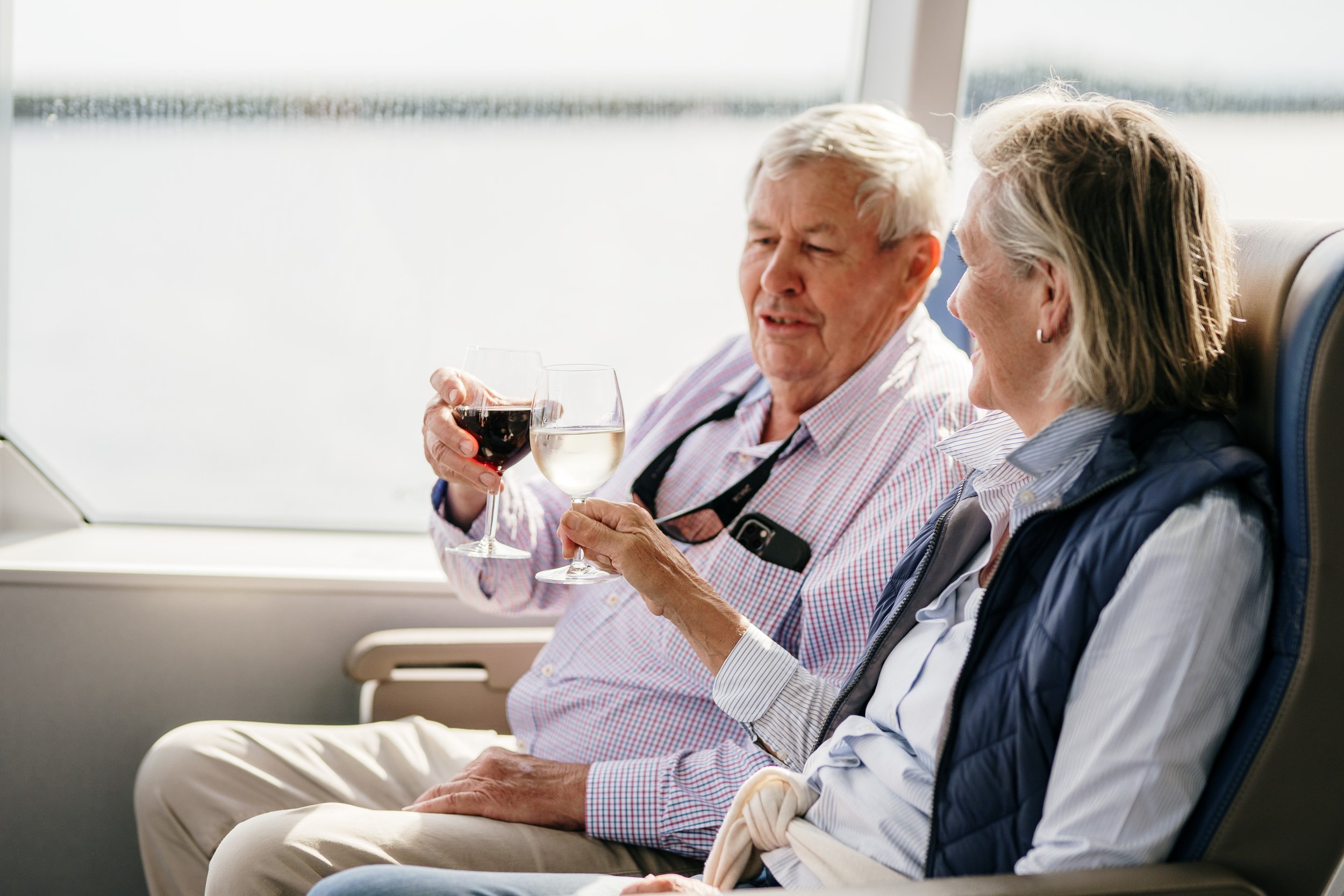 Elderly couple sitting on a boat by a window toasting wineglasses