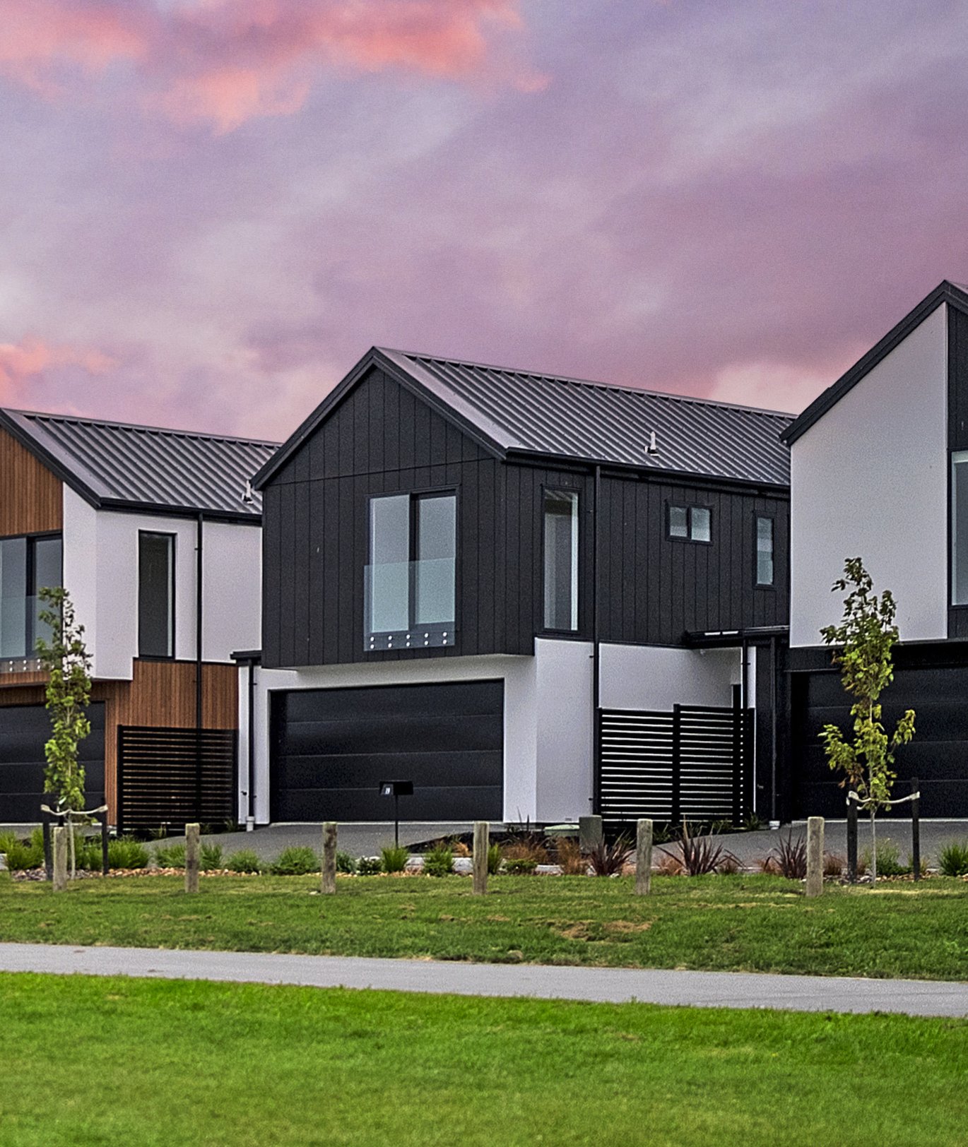 Row of modern duplex houses with black and white facades, large windows, small front yards, and parked cars in front, under a partly cloudy sky.