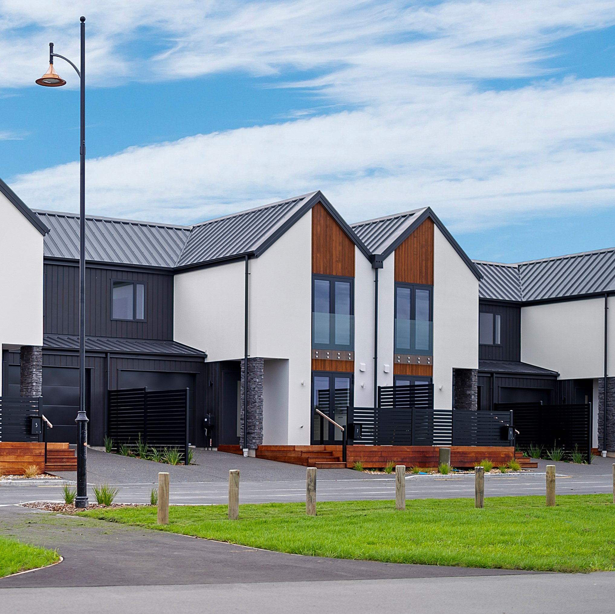 Modern townhouses with black and wood exterior, parked cars in front, and a blue sky with clouds.