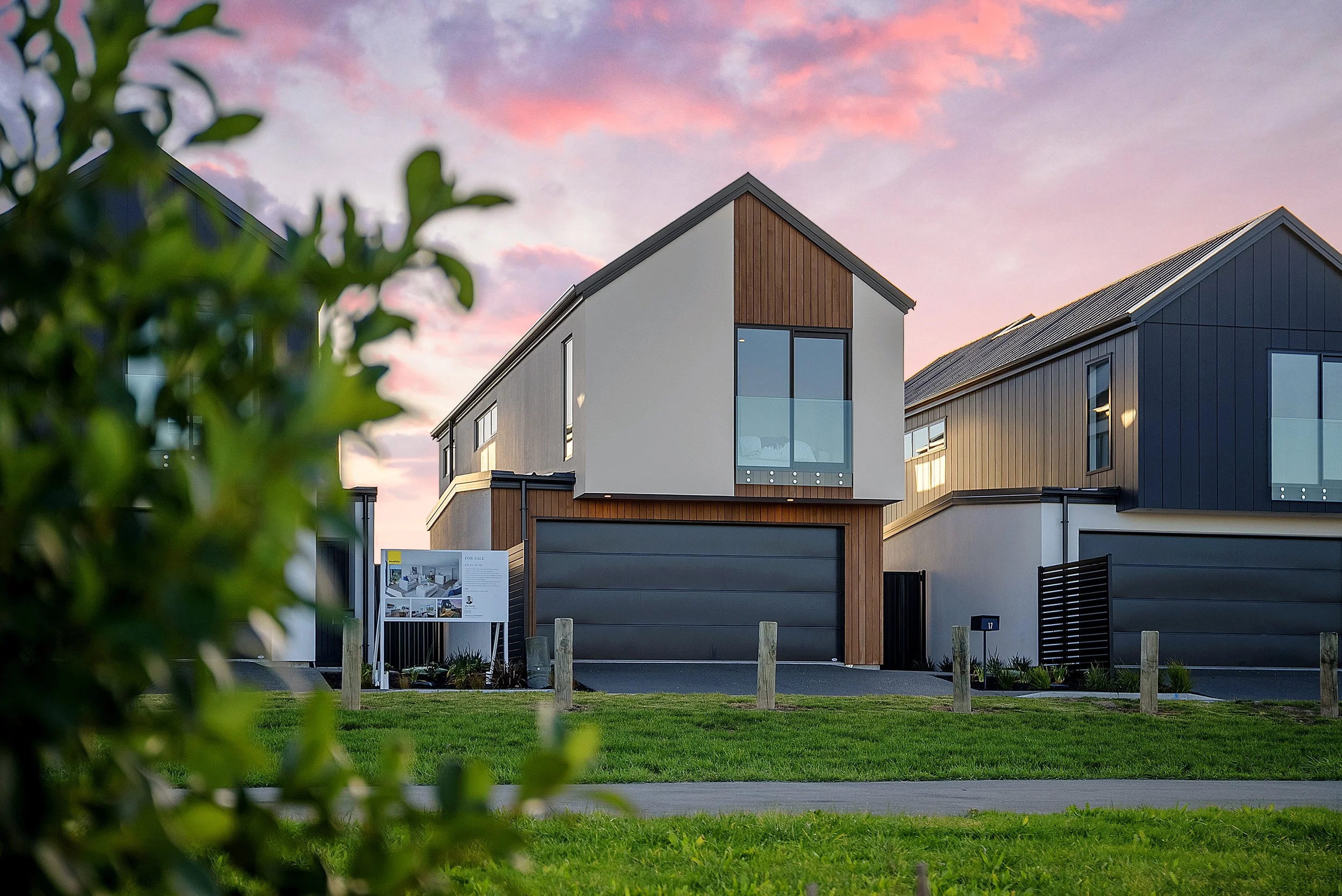 Modern row of three houses with dark and light exterior finishes, large windows, and small front gardens, under a partly cloudy sky.