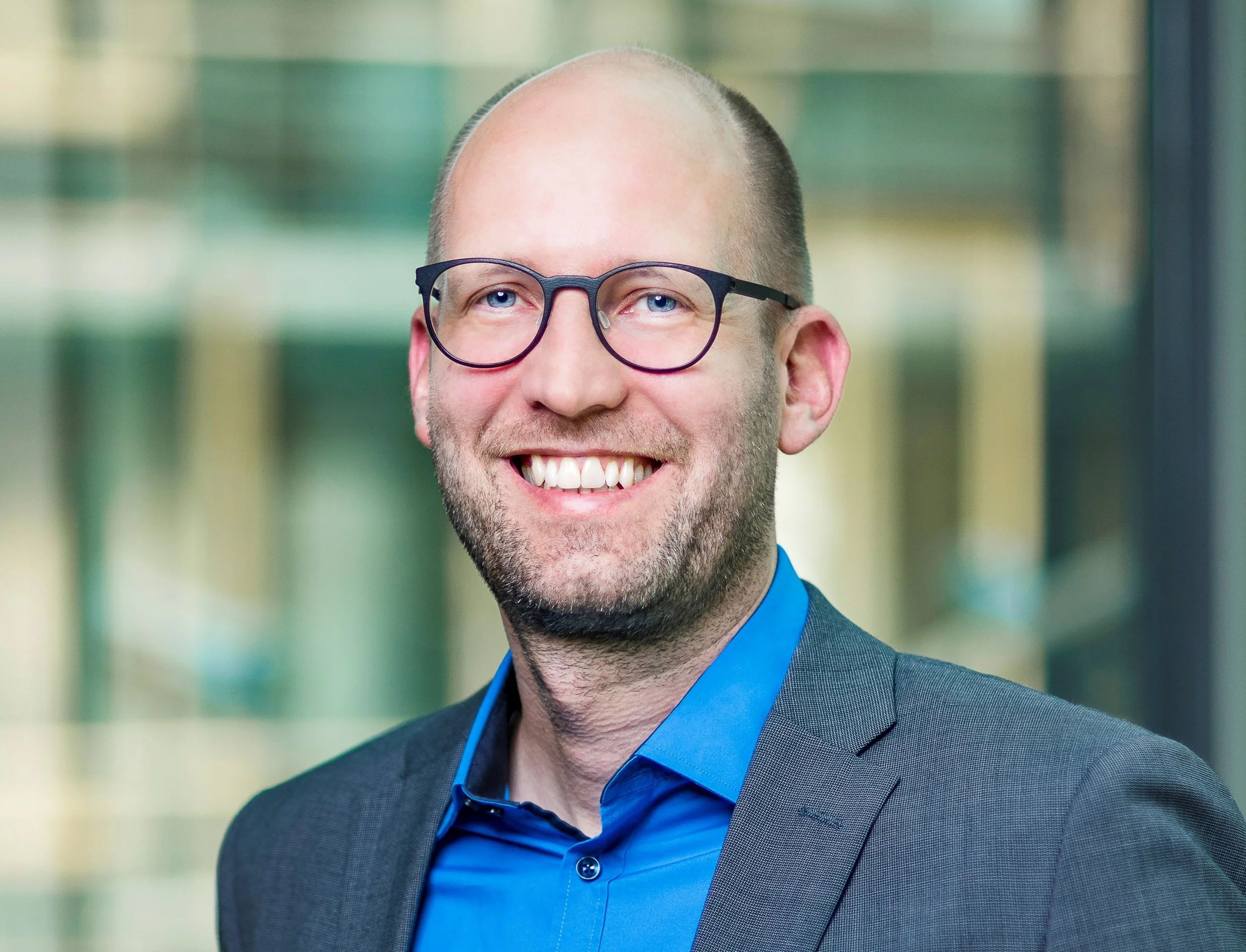 Portrait of Pascal Hetze, Programme Manager at Stifterverband, wearing glasses, a blue shirt and a grey jacket on top