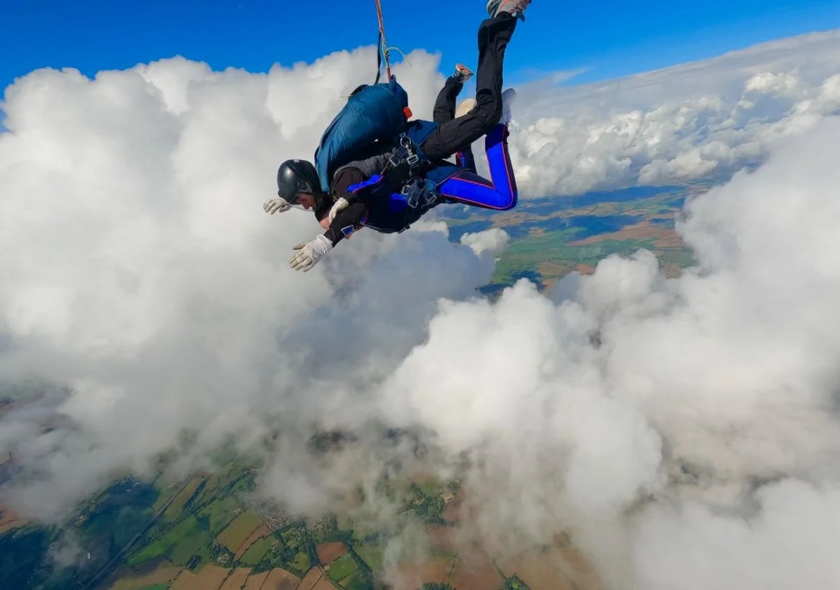 Skydiver in mid-air with a cloudy sky and farmland below.