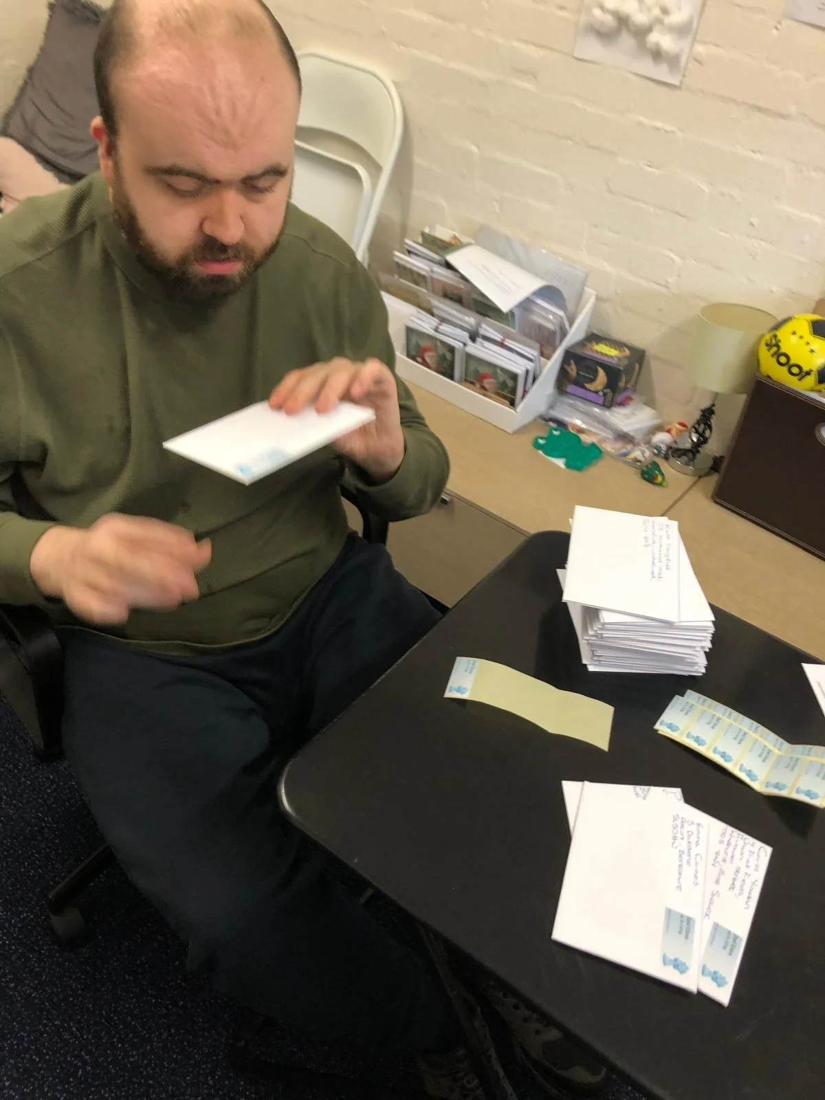 A man sitting at a desk stacking envelopes and stickers with a pile of sealed envelopes in front of him.