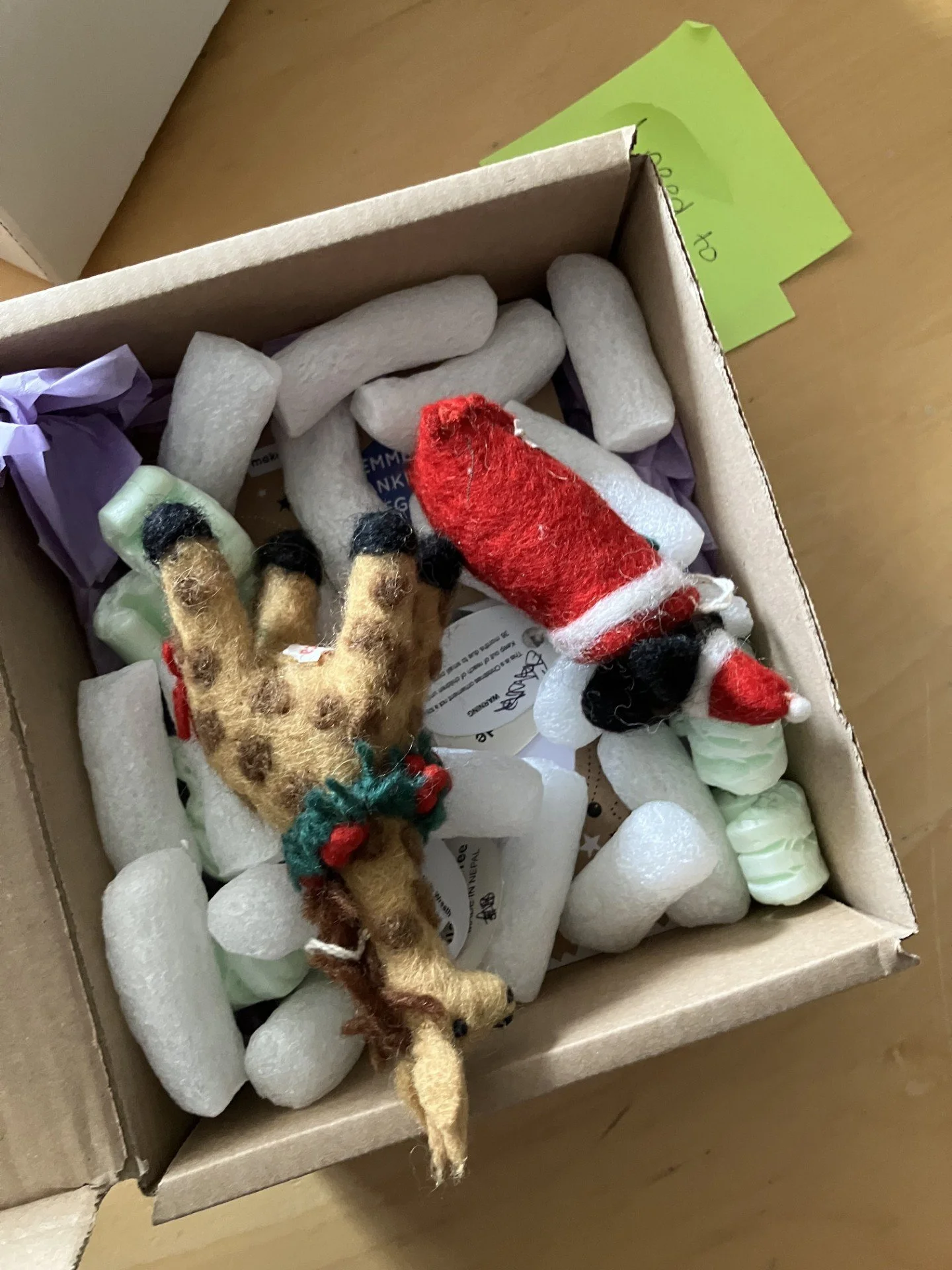 A cardboard box filled with packing peanuts and Christmas-themed decorations, including a felt reindeer and a felt Santa Claus figure.