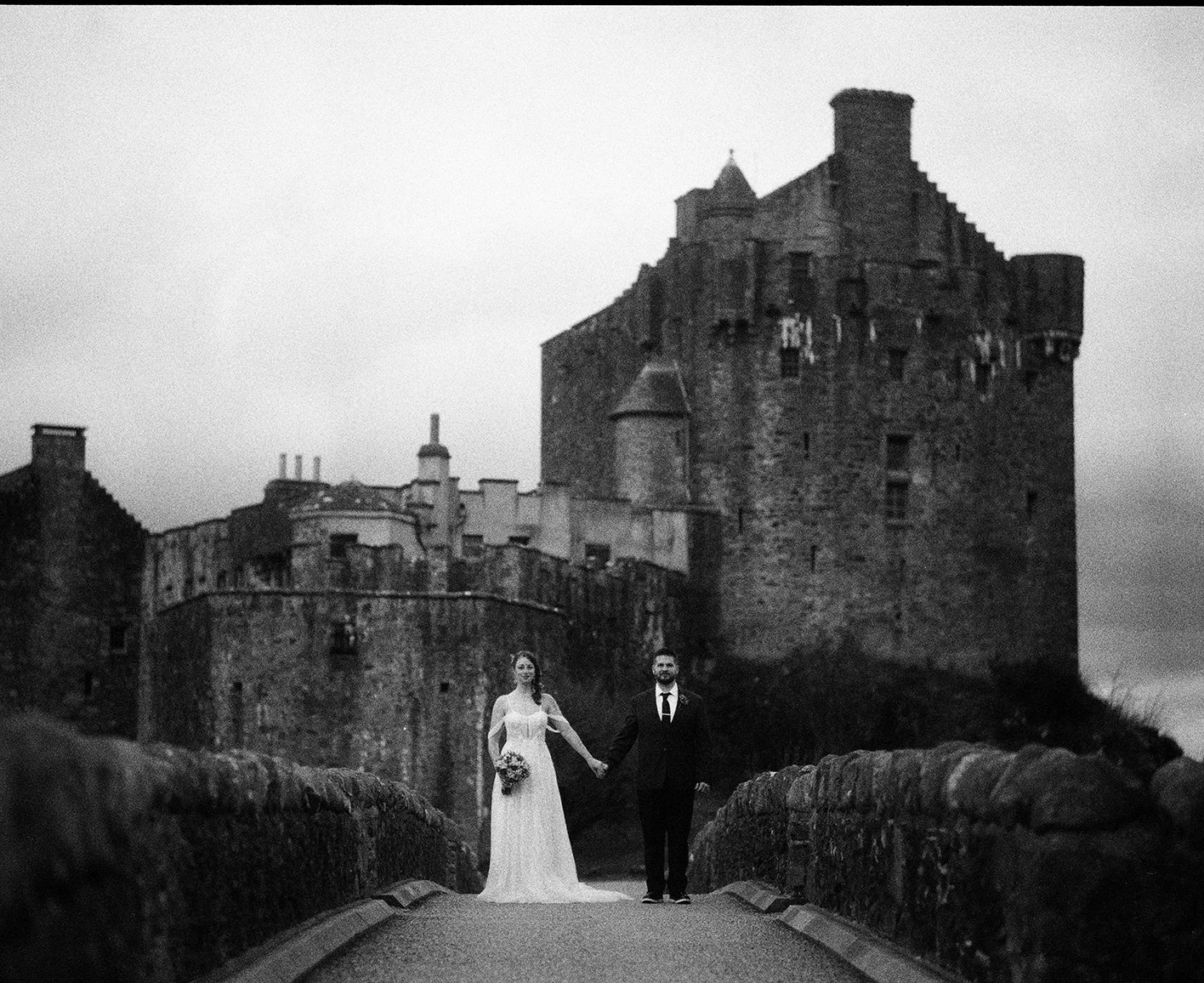 Bride and groom are posing front of the Eilean Donan Castle in Scotland on their Isle of Skye Elopement day