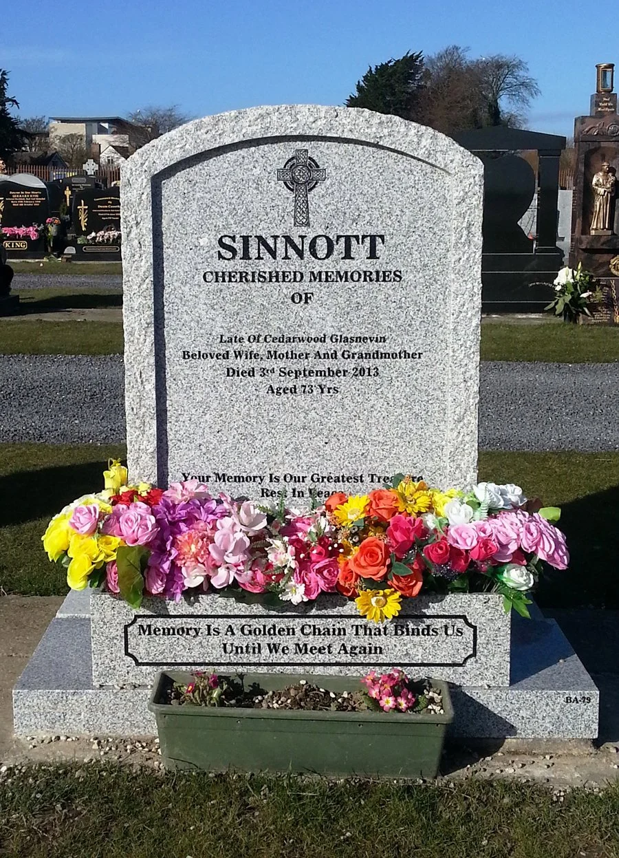 Gravestone with colorful flowers at a cemetery, engraved with the name Sinnott and a memorial message.