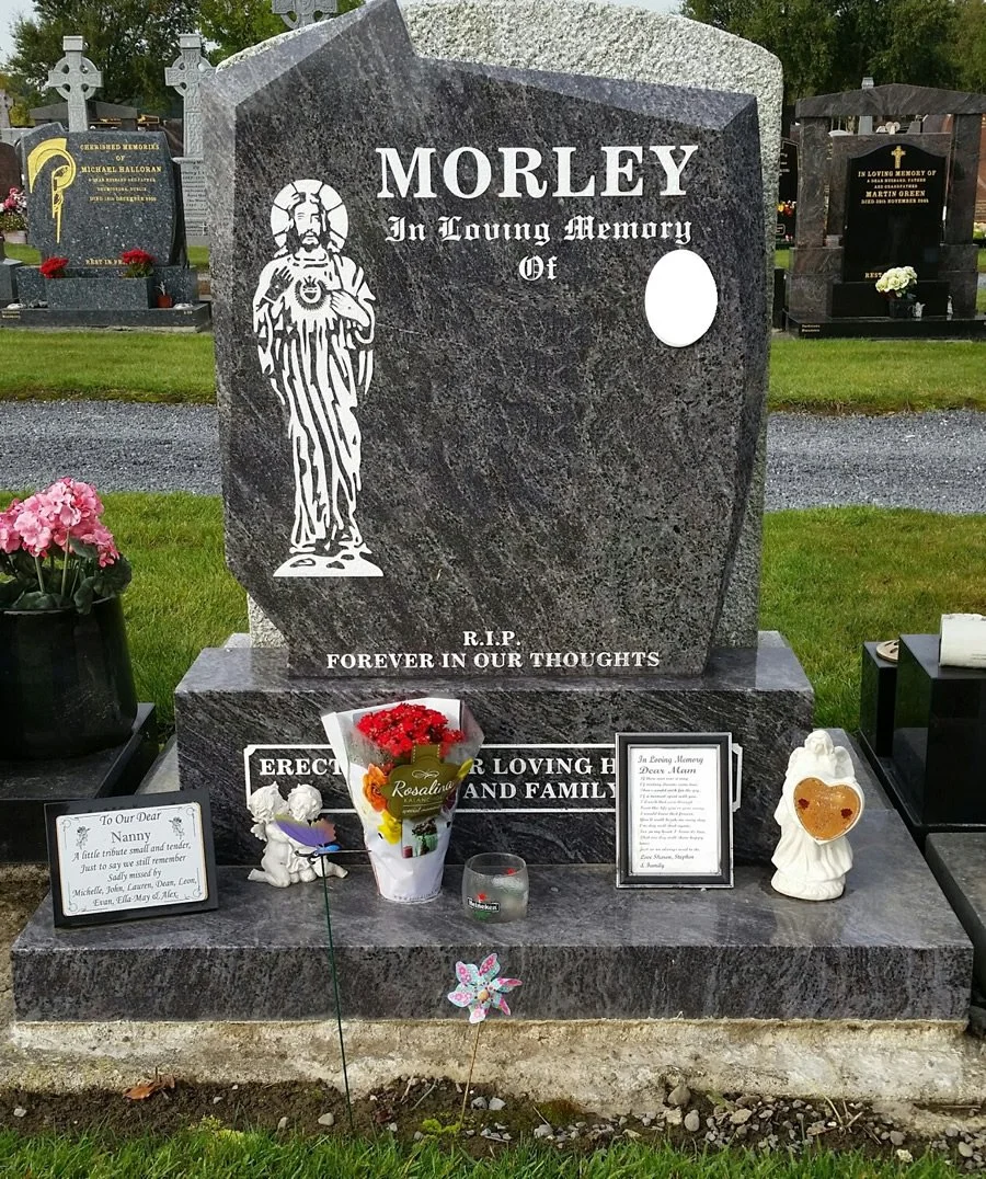 Gravestone for Morley in a cemetery with flowers, notes, and religious symbols.