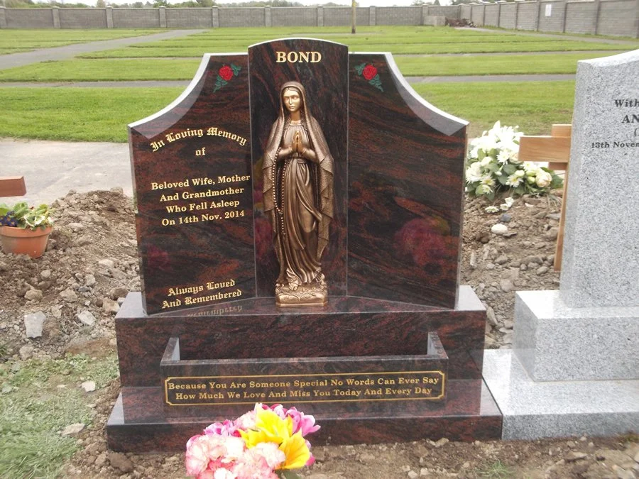 Gravestone with a religious statue of the Virgin Mary in the center, engraved with inscriptions in memory of a beloved wife, mother, and grandmother, and a heartfelt message of love and remembrance, surrounded by flowers.