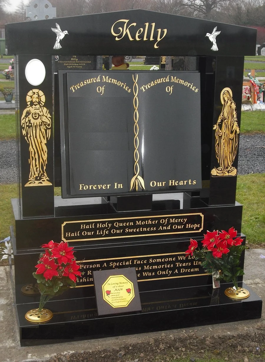 Gravestone with the name Kelly, adorned with religious symbols and images of Jesus and the Virgin Mary, decorated with red poinsettias, in a cemetery.