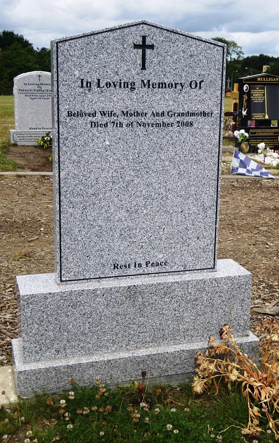 Gravestone in a cemetery with an inscription honoring a woman who died on November 7, 2008, with a cross at the top and a peaceful message at the bottom.
