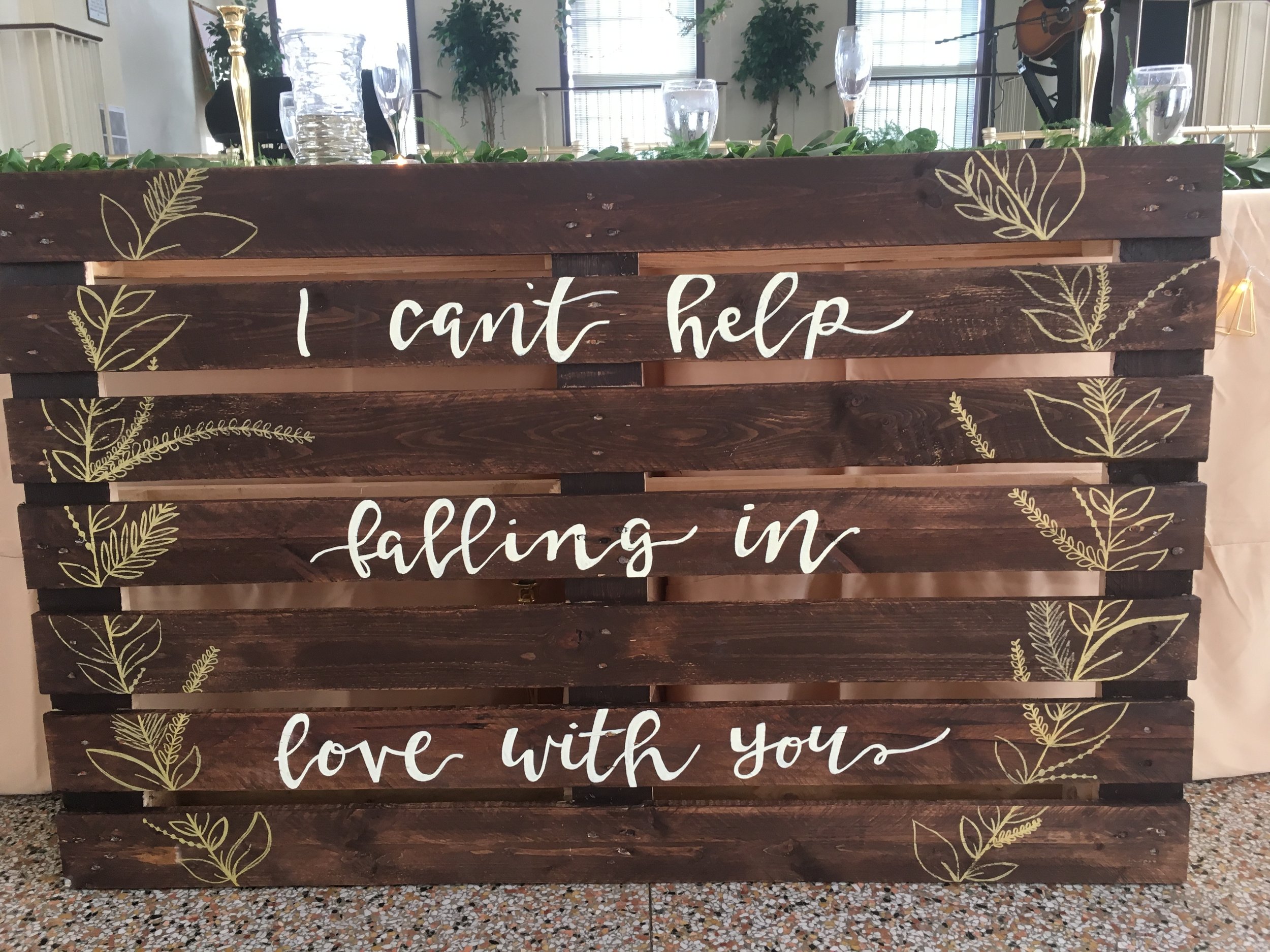 Decorative wooden pallet sign with gold leaf designs and the handwritten phrase 'I can't help falling in love with you'