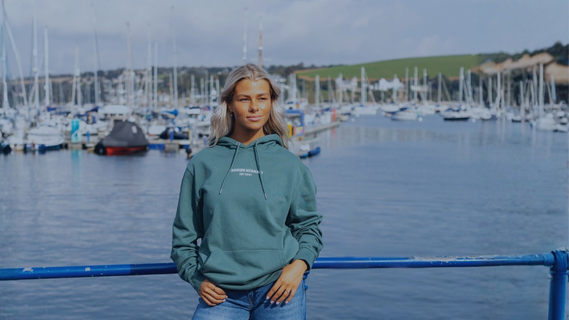 A girl by a harbour in Cornwall wearing a green hoodie by Cornish Mermaid