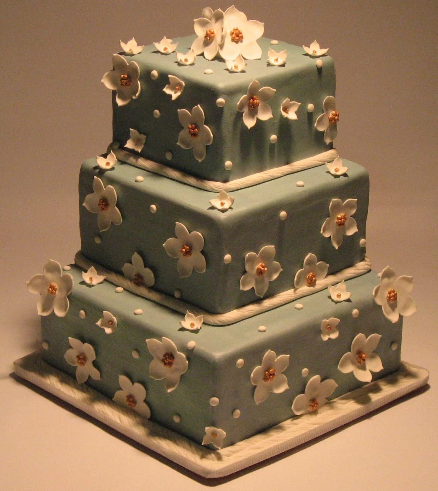 Simple Cakes for Weddings and Events, a light blue cake with ornamental, edible flowers and white lining.