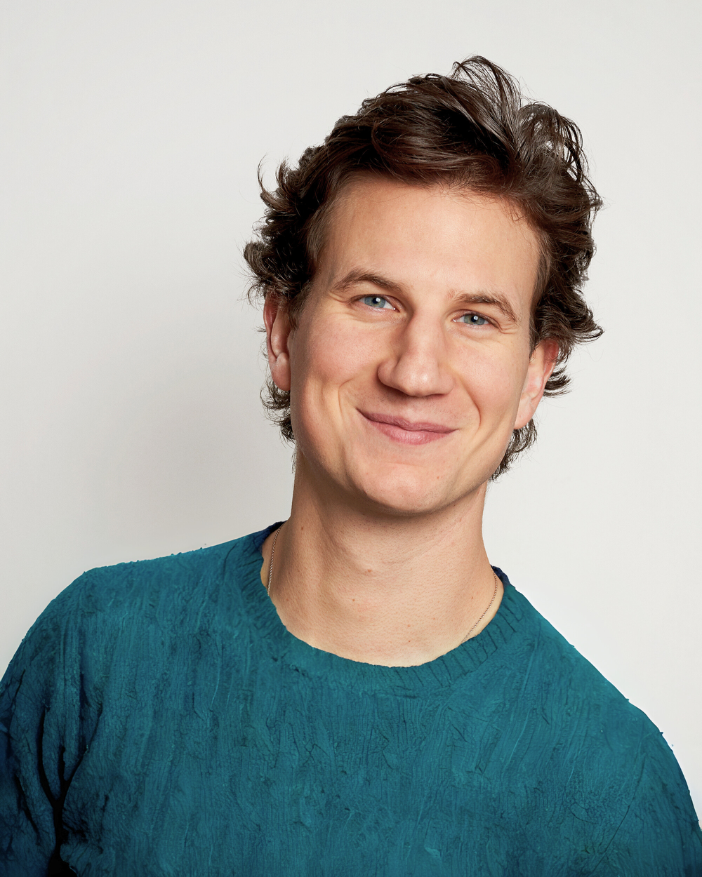 Andrew Rowe headshot, smiling, in a teal jumper