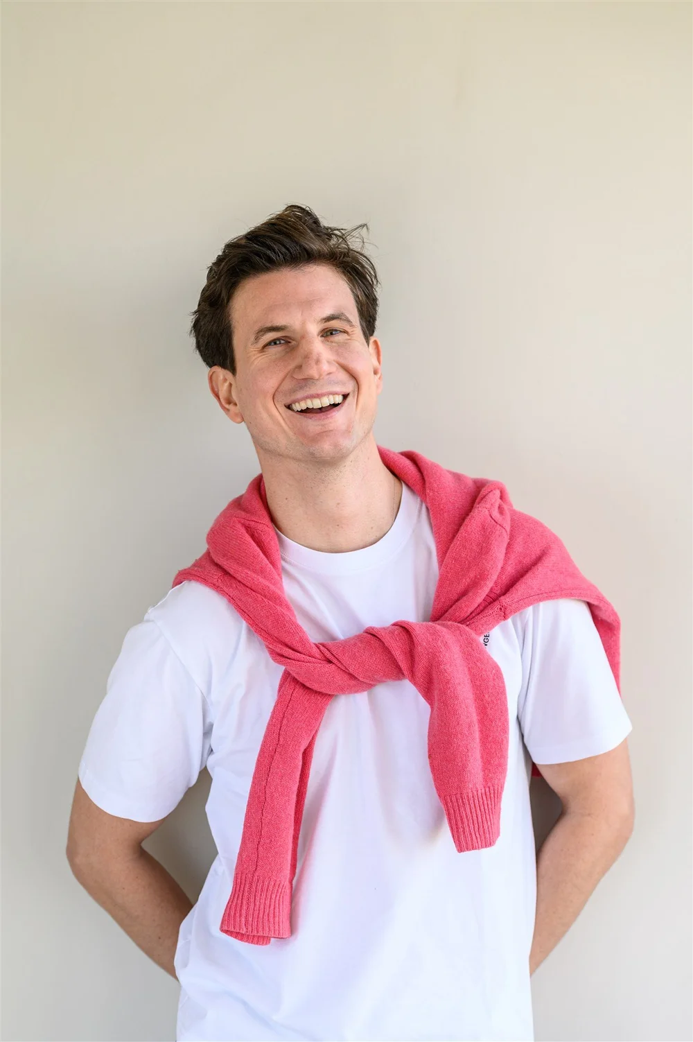 Andrew Rowe smiling, wearing a white t-shirt with a pink jumper over his shoulders