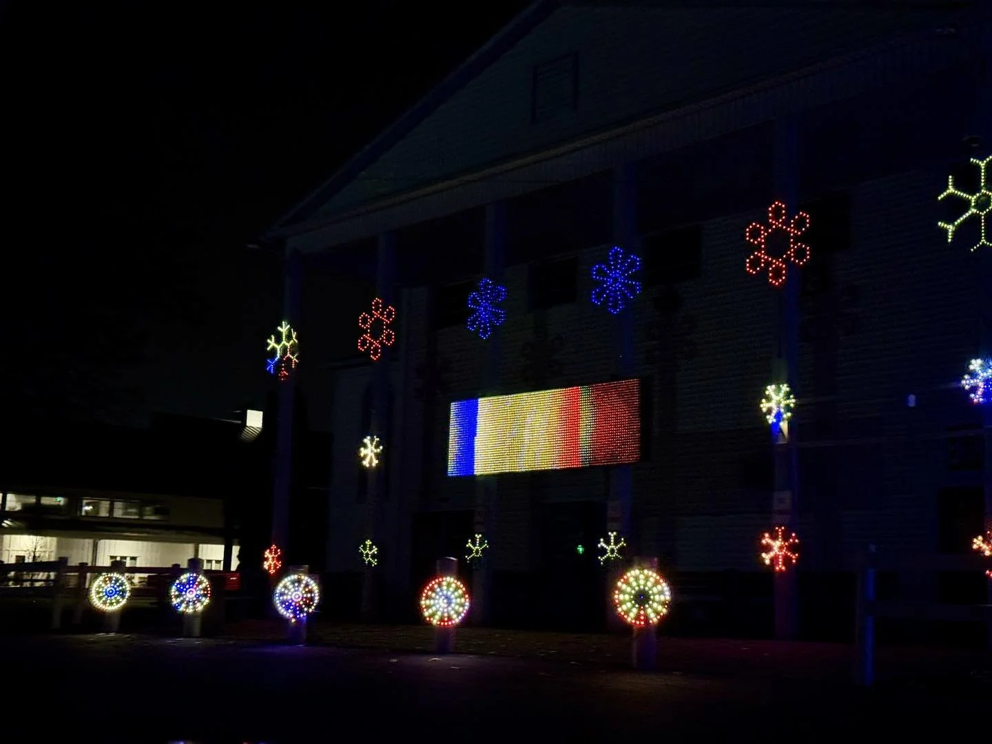 Dark building adorned with colorful LED holiday decorations including snowflakes and circular patterns, with an LED display screen in the center showing rainbow colors.