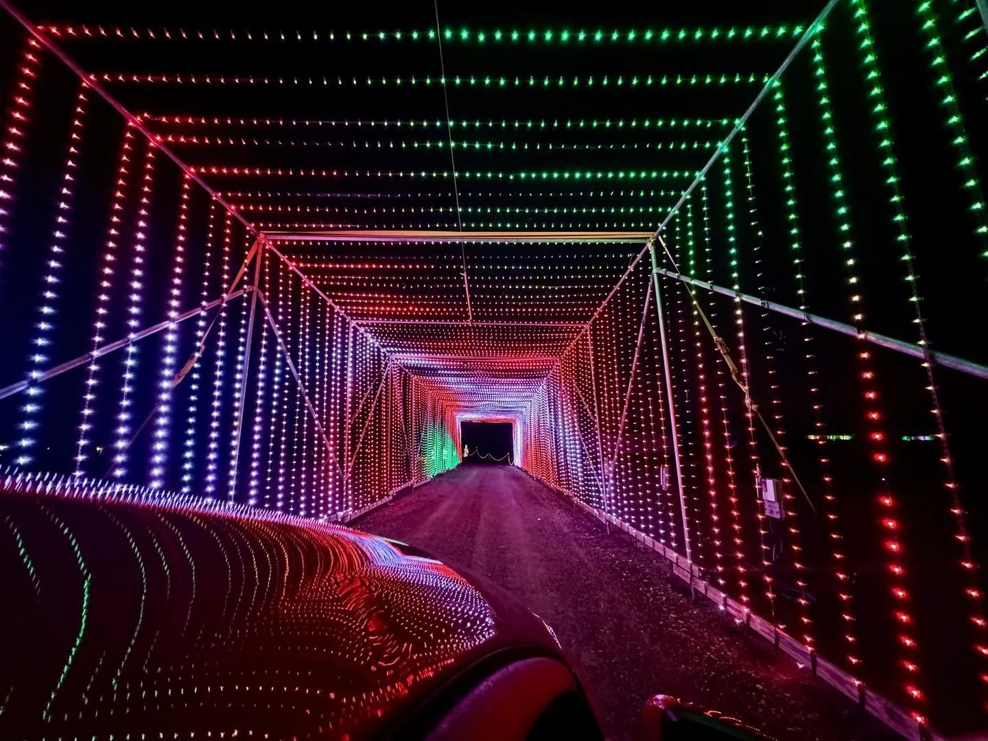 Colorful LED light tunnel with red, green, and white lights creating a patterned pathway, viewed from a car inside the tunnel at night.
