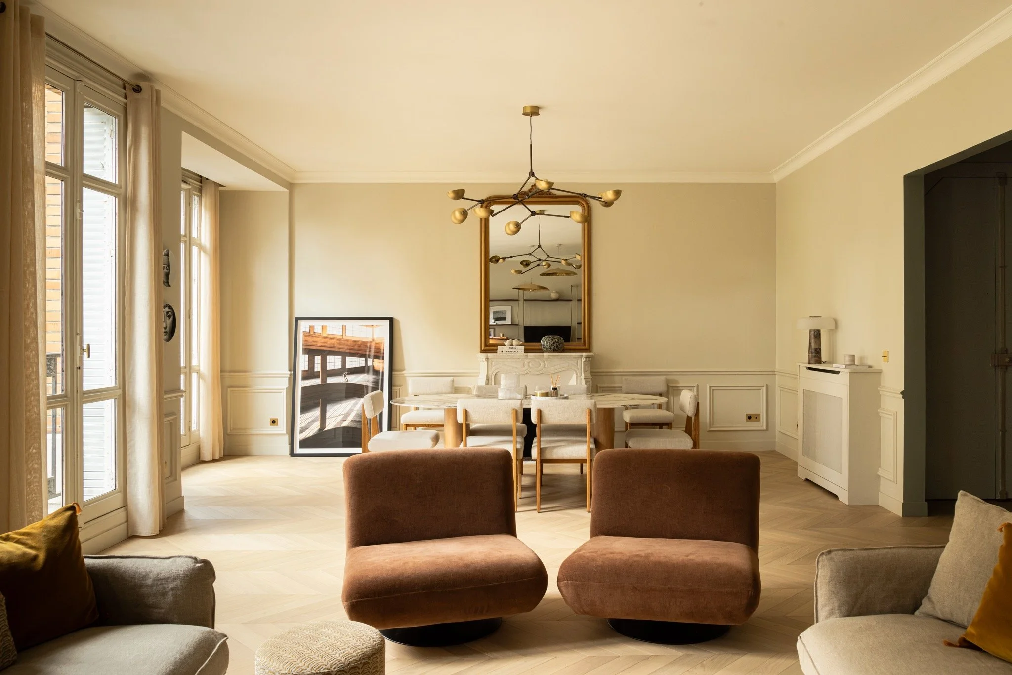 La Muette apartment in Paris 16th by Yasmine B Design, with terracotta lounge chairs opening onto a dining area with a fireplace and tall mirror.