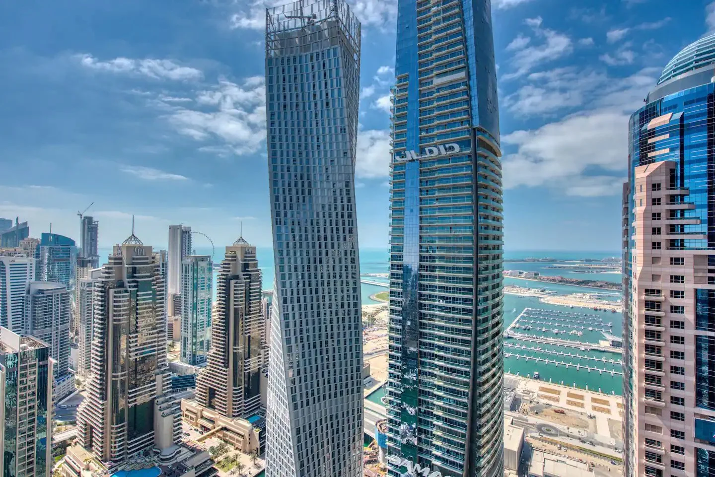 Dubai skyline with tall glass towers in the foreground and harbour berths and open sea beyond.