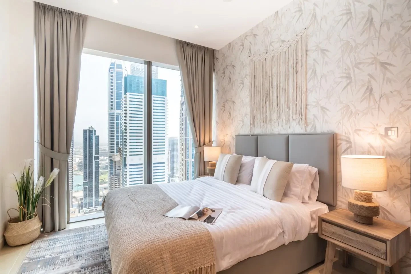 Neutral Dubai bedroom by Yasmine B Design with leaf-patterned wallpaper, a fringed wall hanging and full-height curtains.