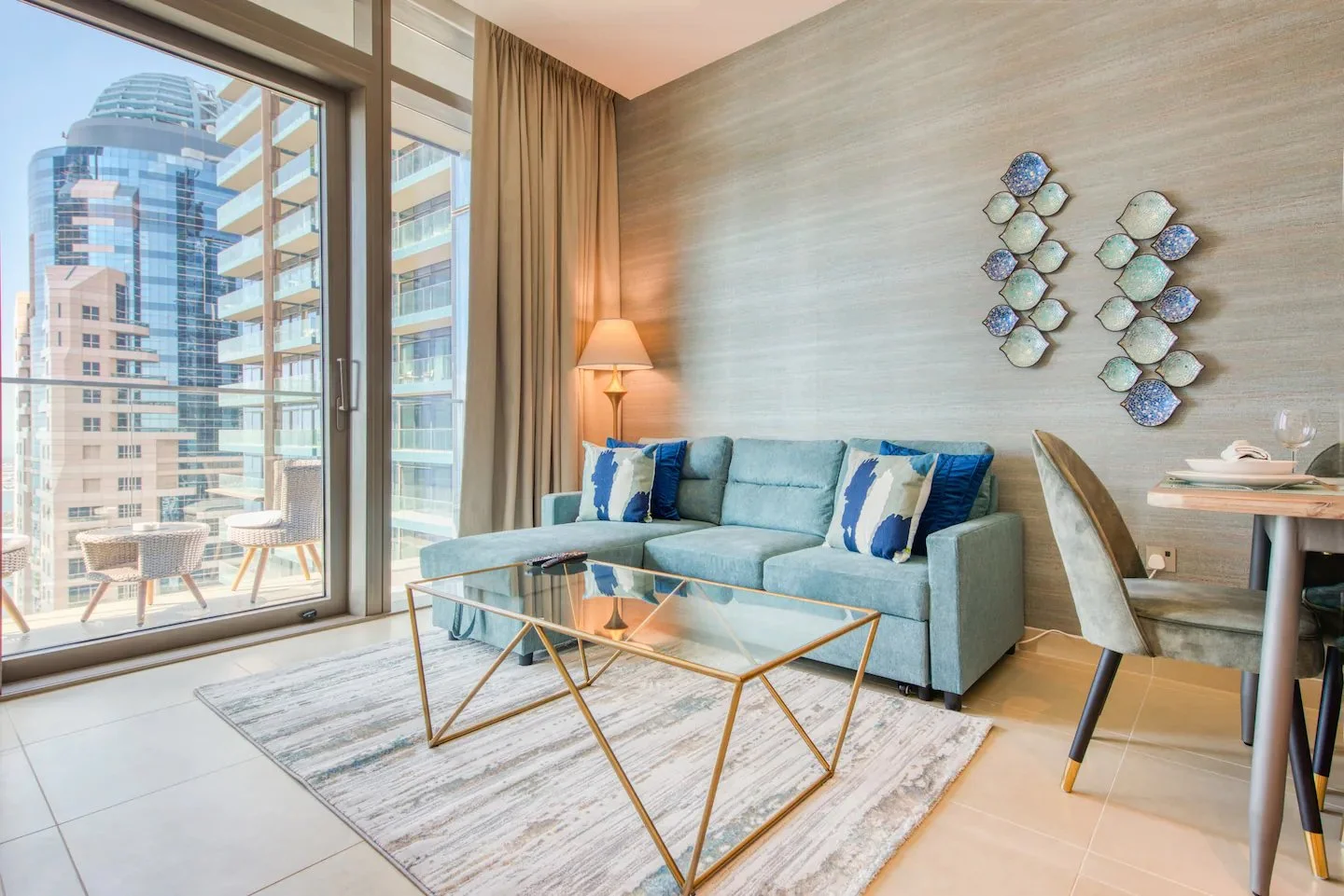 Dubai Marina living room by Yasmine B Design with a pale blue corner sofa, glass coffee table and blue wall decorations.