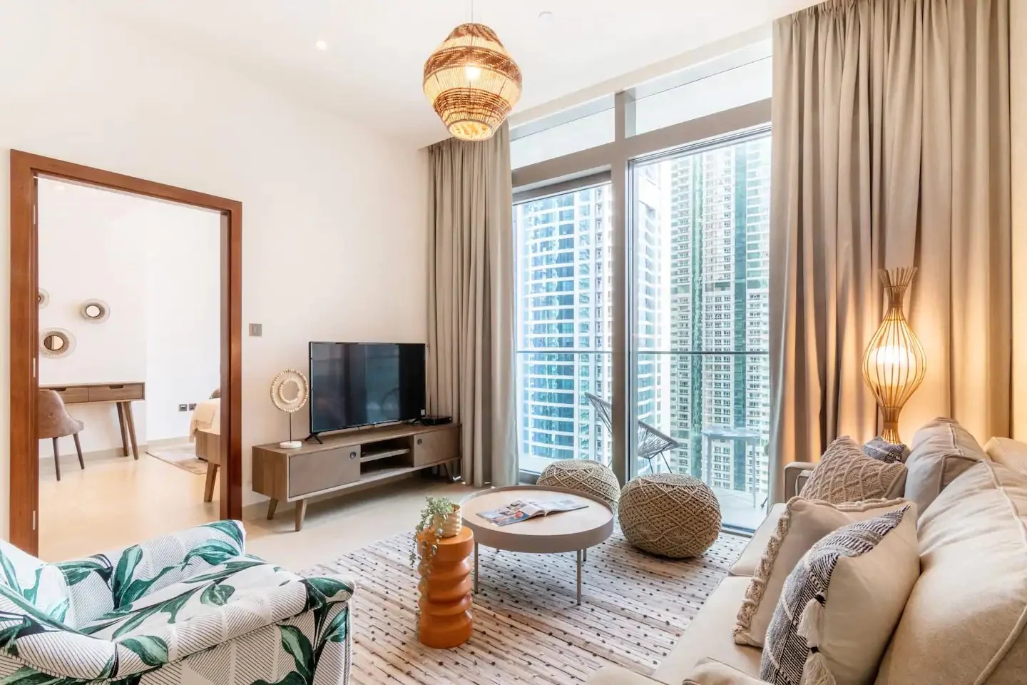 Dubai living room with a cream sofa, botanical-print armchair, woven lighting and two round pouffes beside the balcony.