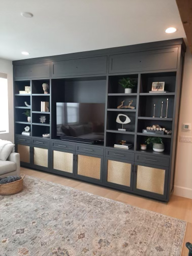 Black built-in entertainment center with shelves and cabinets, a flat-screen TV, decorative items, plants, and framed photos in a living room.