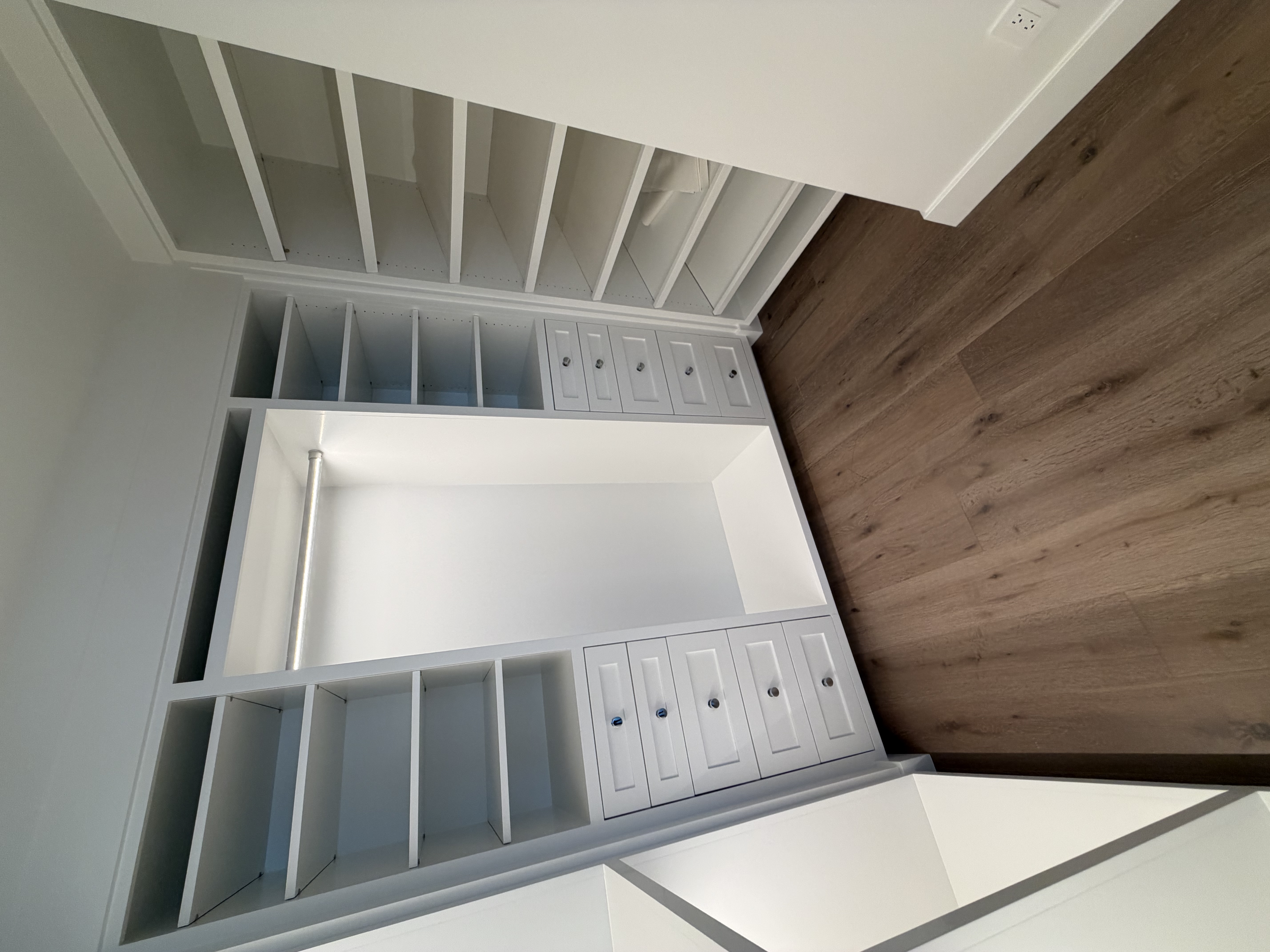 Empty white built-in closet with shelves and drawers in a room with wooden floor.