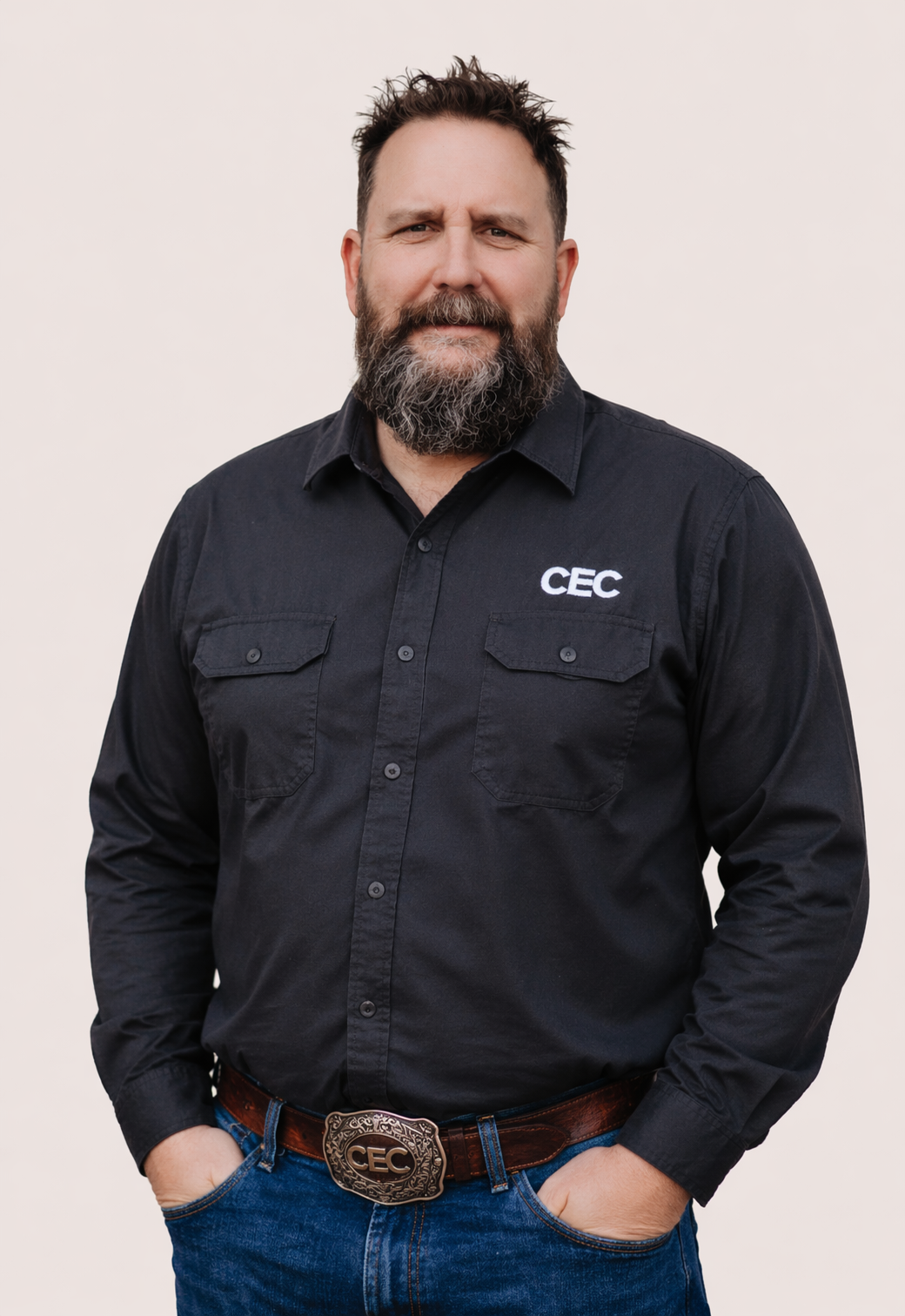 A bearded man in a plaid yellow shirt sitting at a table with a city skyline at sunset in the background.