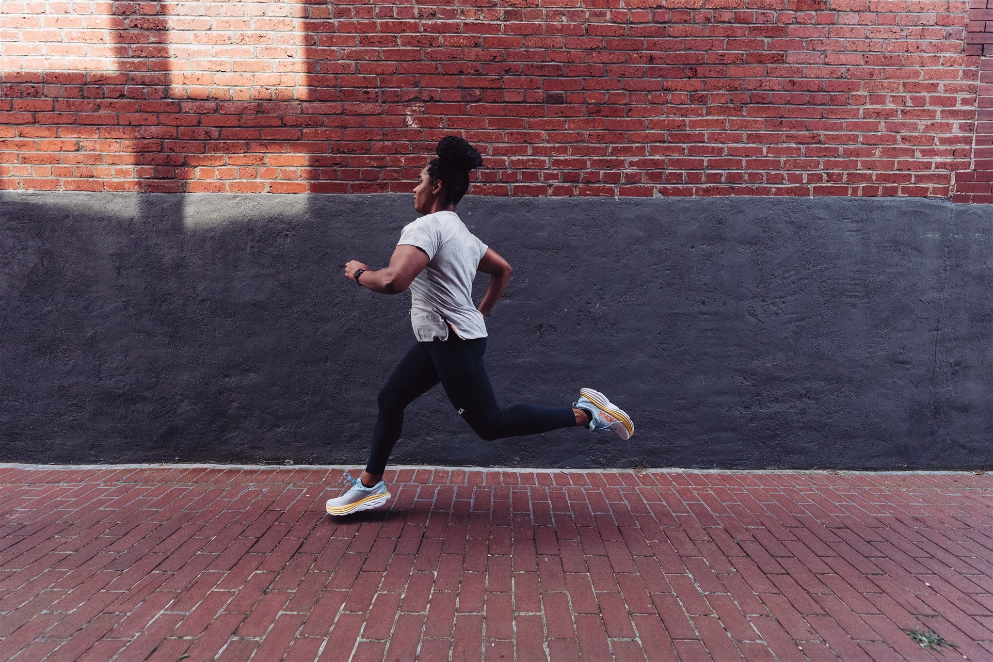A woman running on a brick sidewalk against a brick wall with a black painted lower section