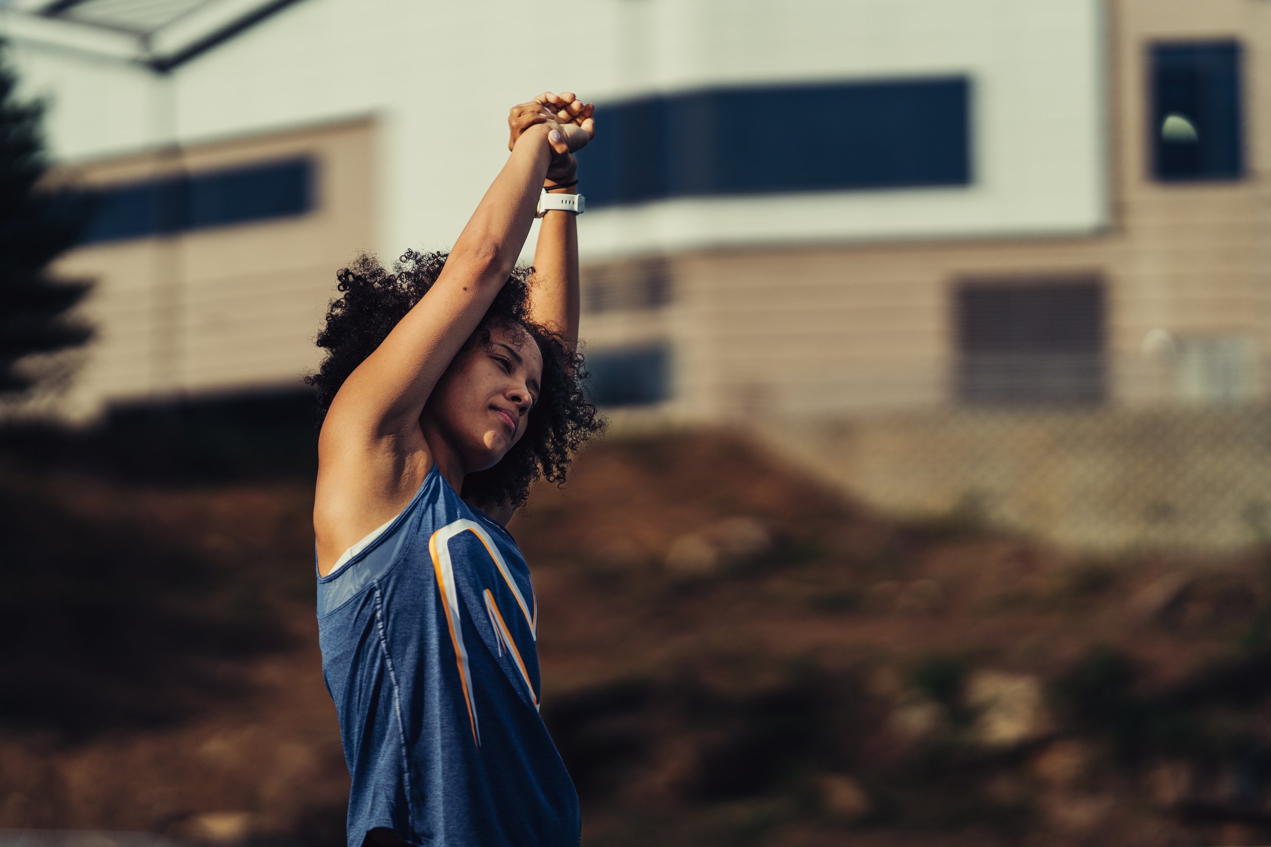 Young woman stretching outdoors in athletic wear on a sunny day.