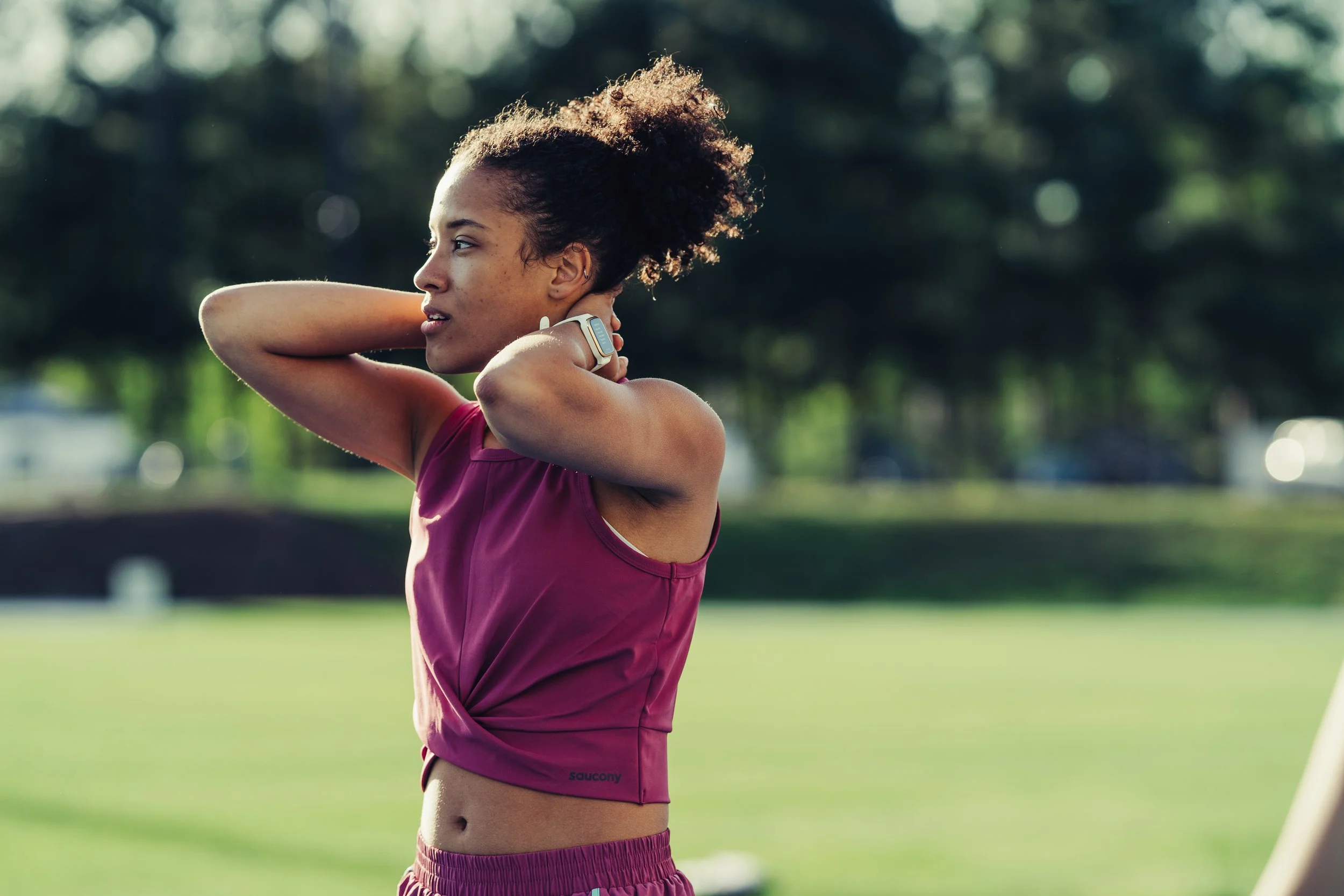 A young woman in athletic clothes adjusting her sports watch outdoors on a sunny day.