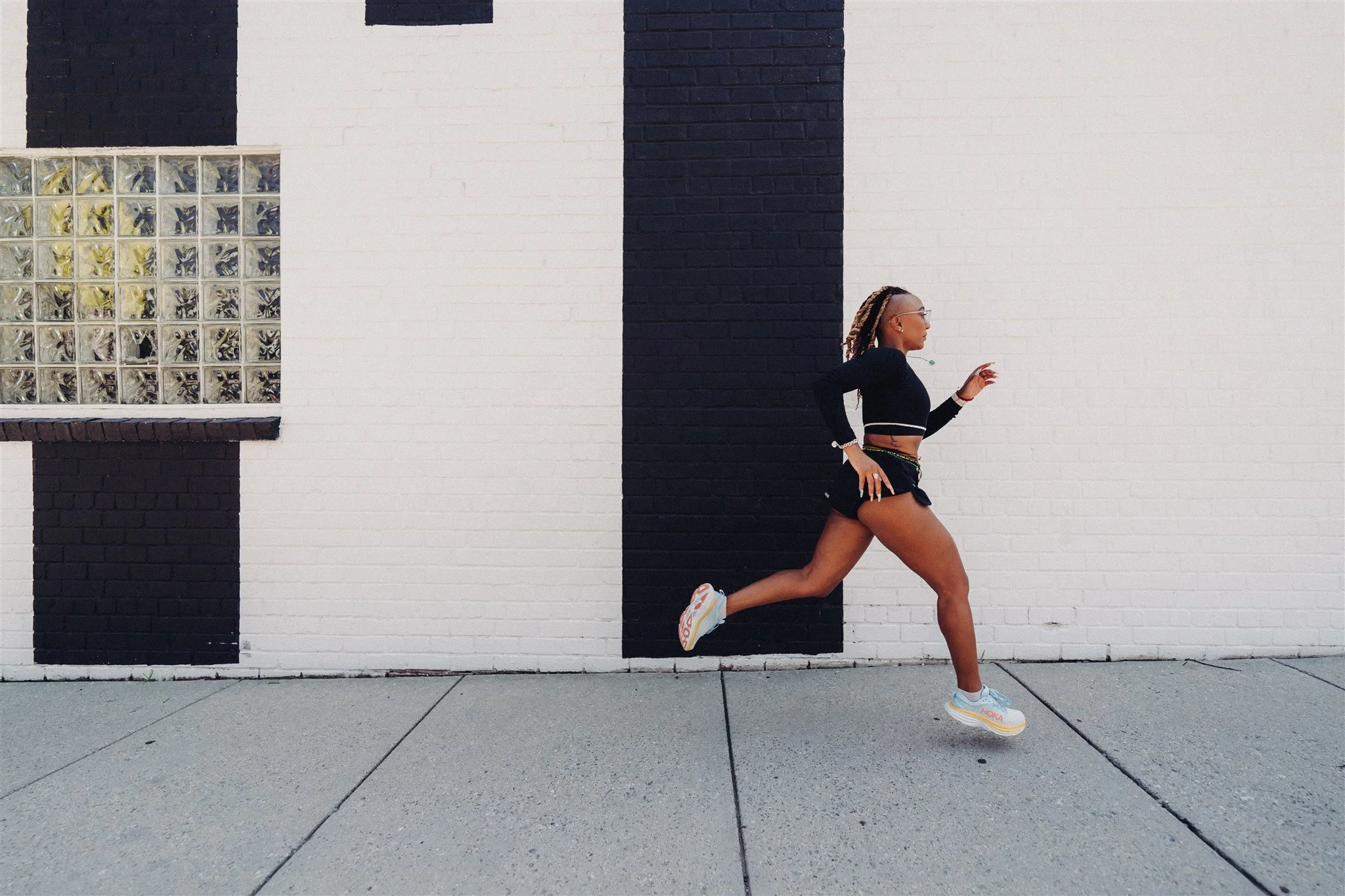 A woman running on the sidewalk in front of a white wall with black vertical stripes.
